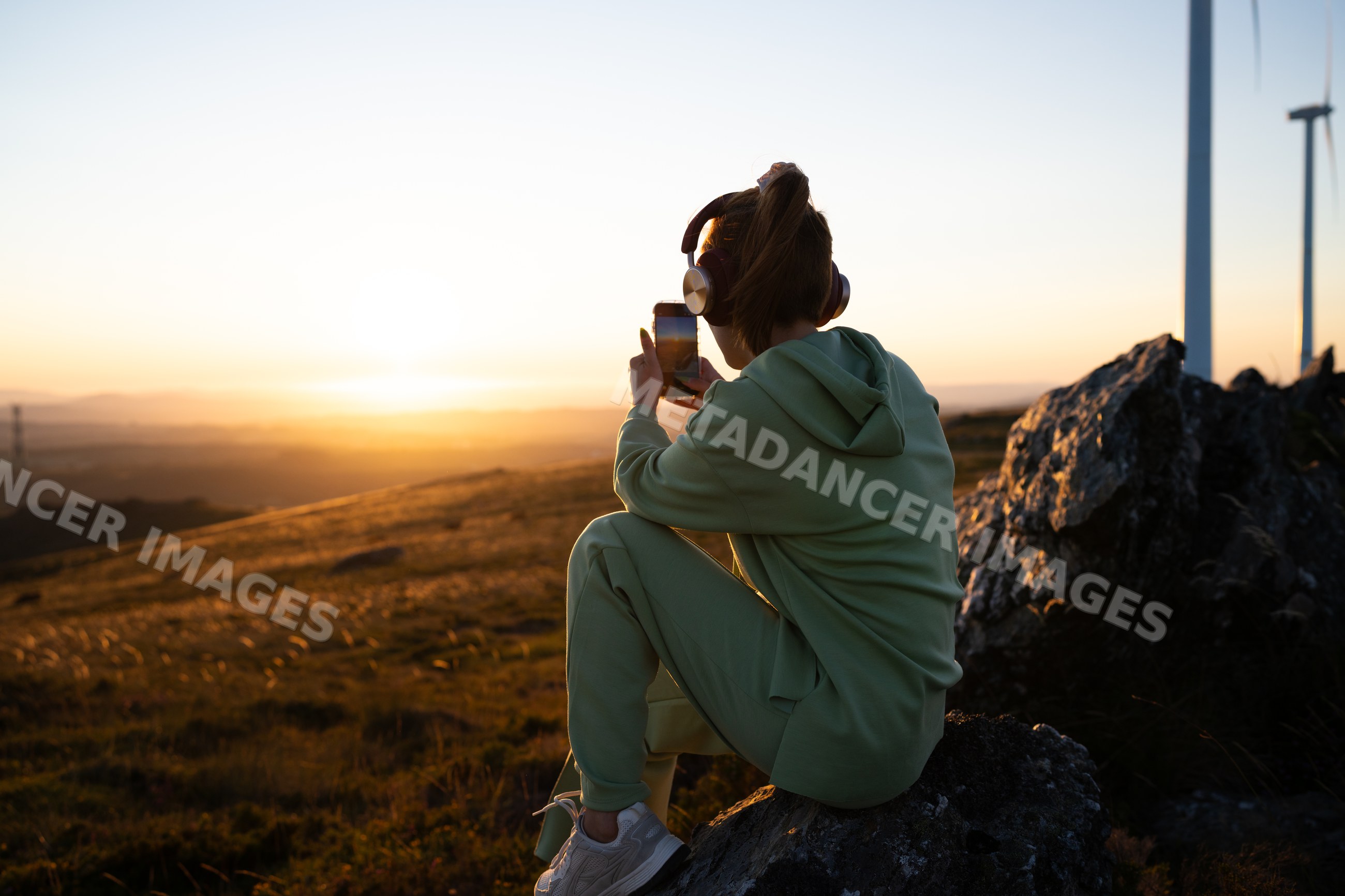 A white woman takes a photo at sunset near wind turbines in Galicia