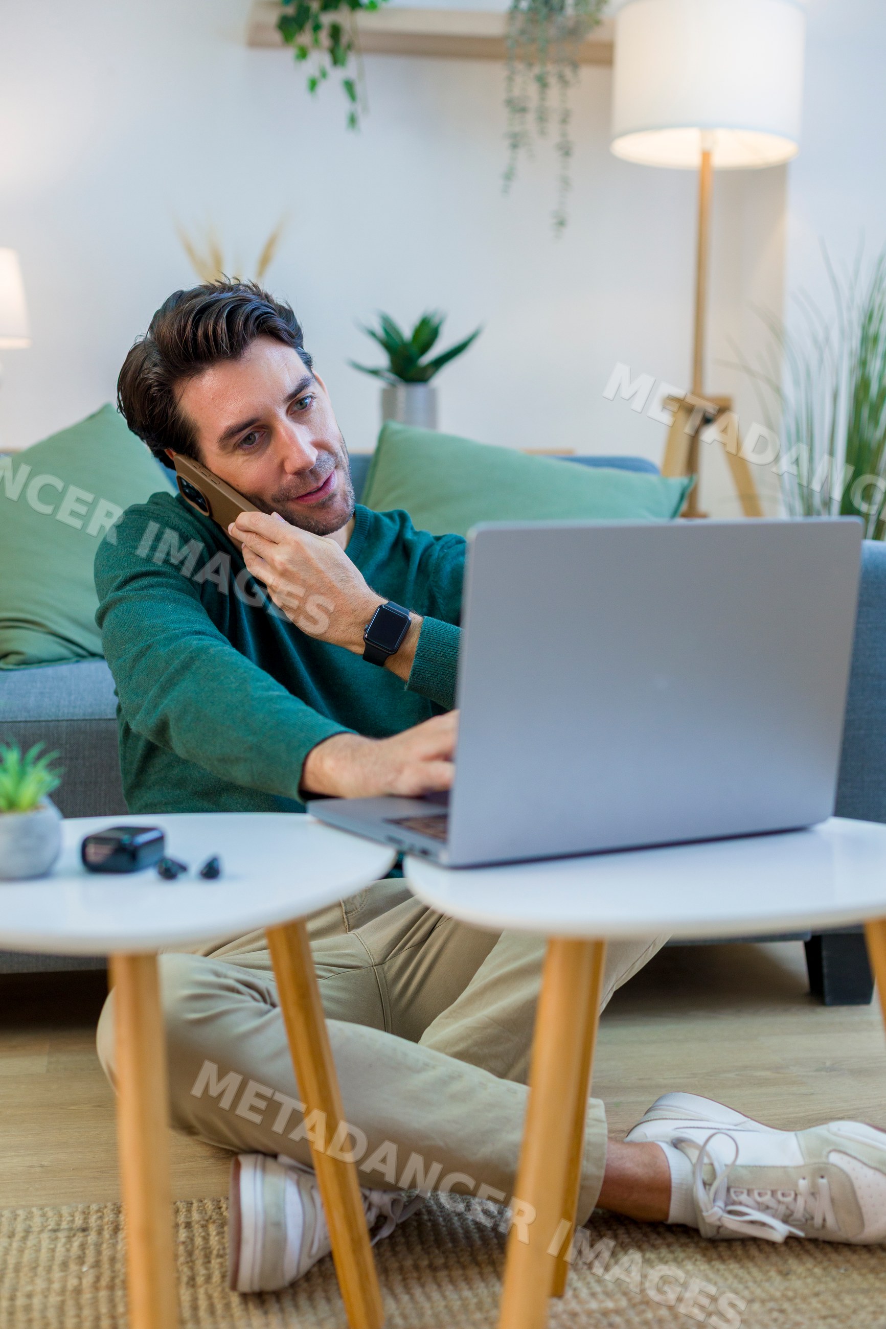White man multitasking with laptop and phone in home living room
