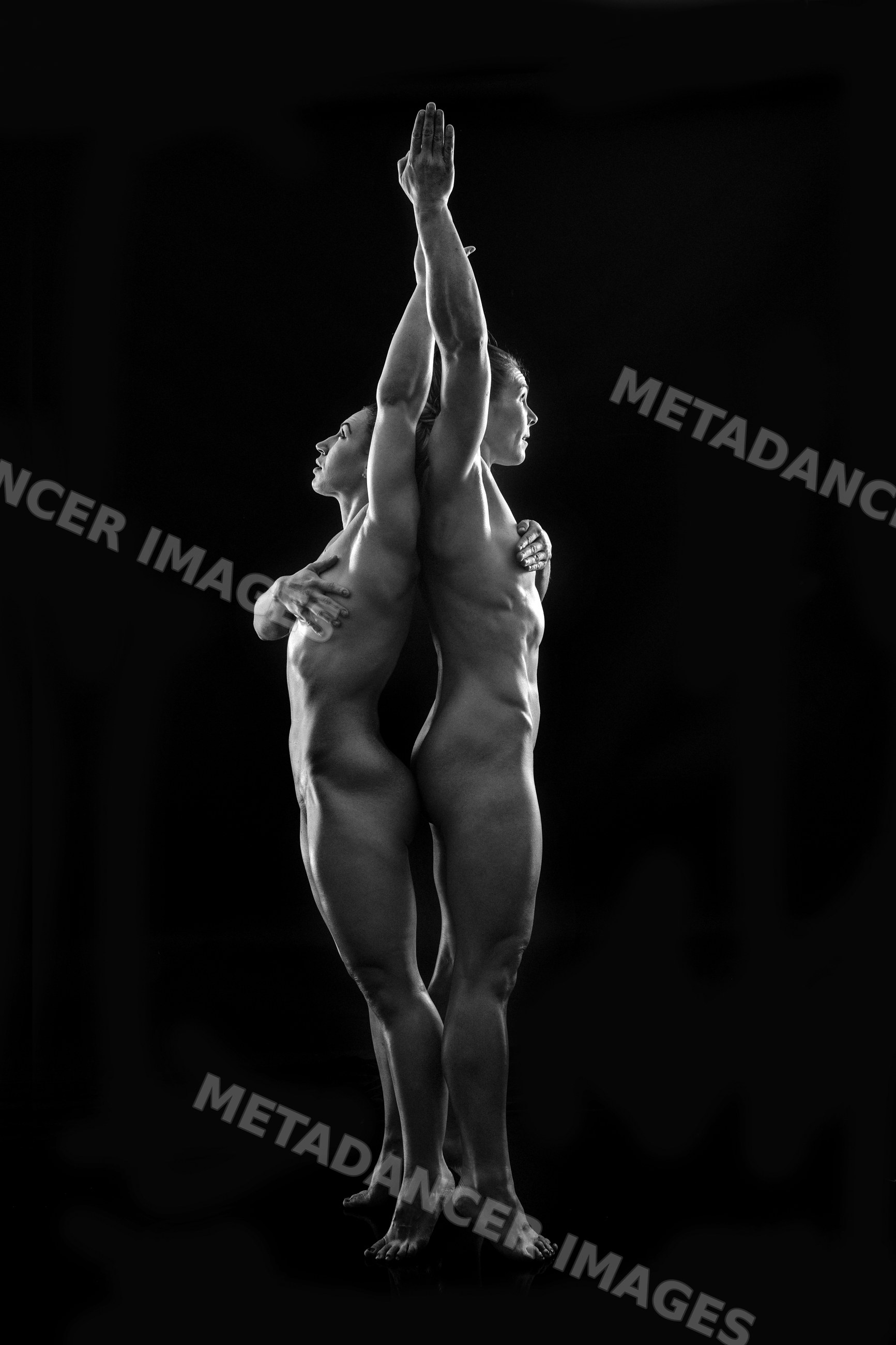 Two white women practicing partner acrobatics yoga in standing pose