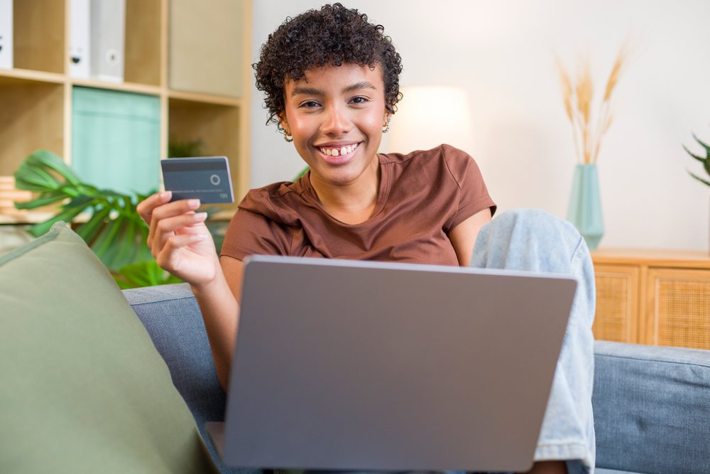 African American woman holding credit card using laptop on sofa