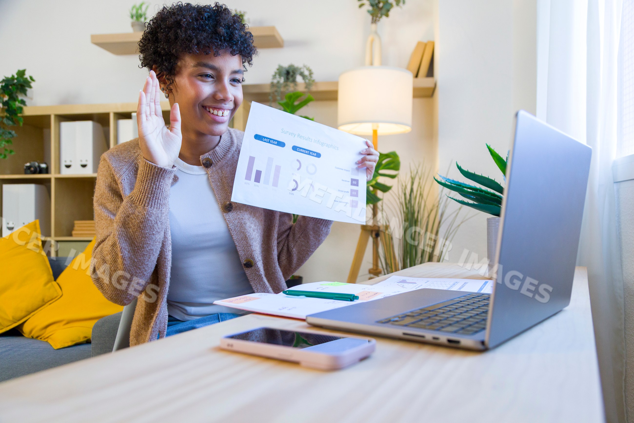 African American woman in home office waving during remote video call