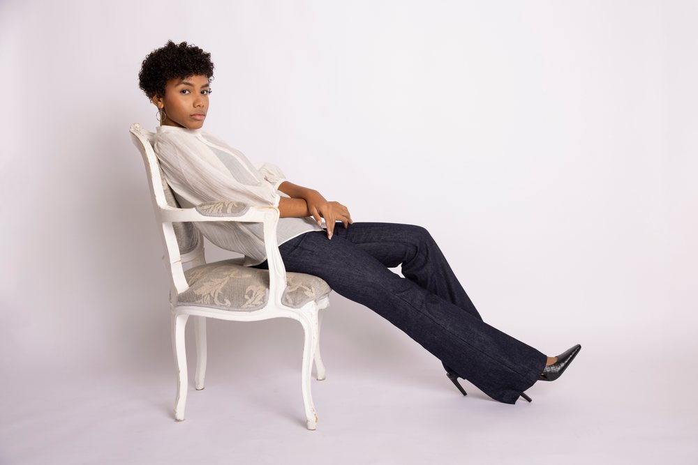 Young Hispanic woman sitting on vintage chair in fashion studio