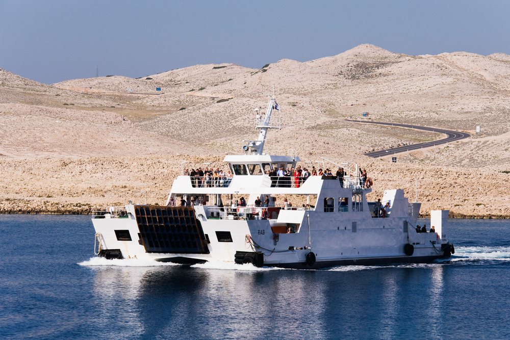 Ferry boat filled with passengers sailing near rocky coastal hills