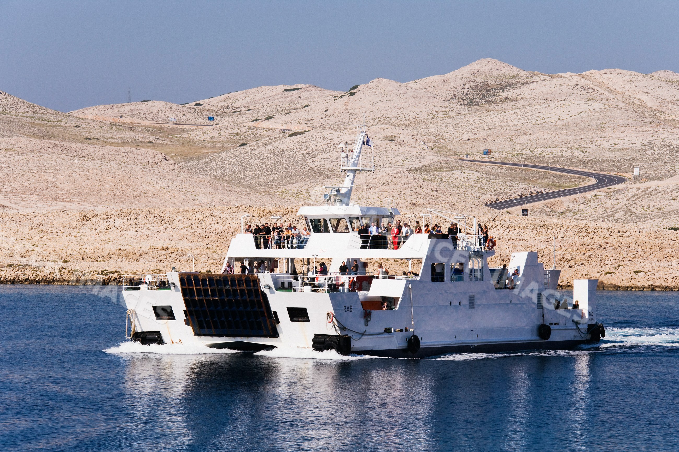 Ferry boat filled with passengers sailing near rocky coastal hills