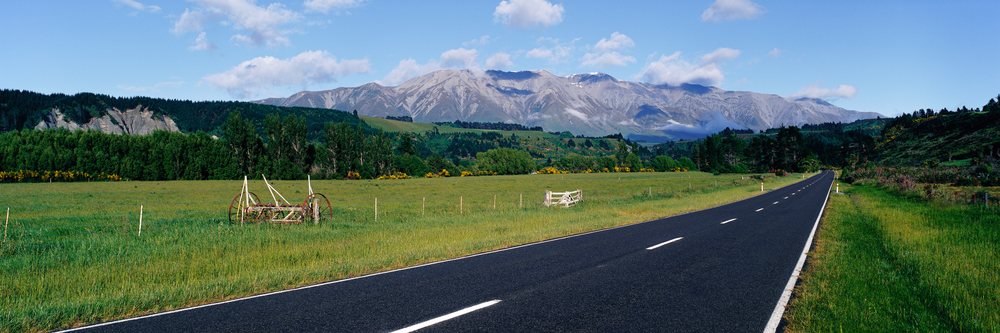 Road through green countryside with mountain range under blue sky