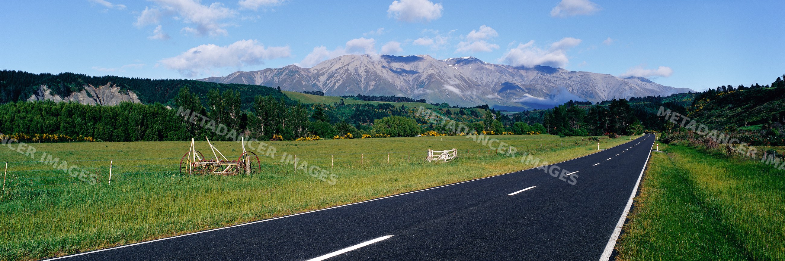 Road through green countryside with mountain range under blue sky