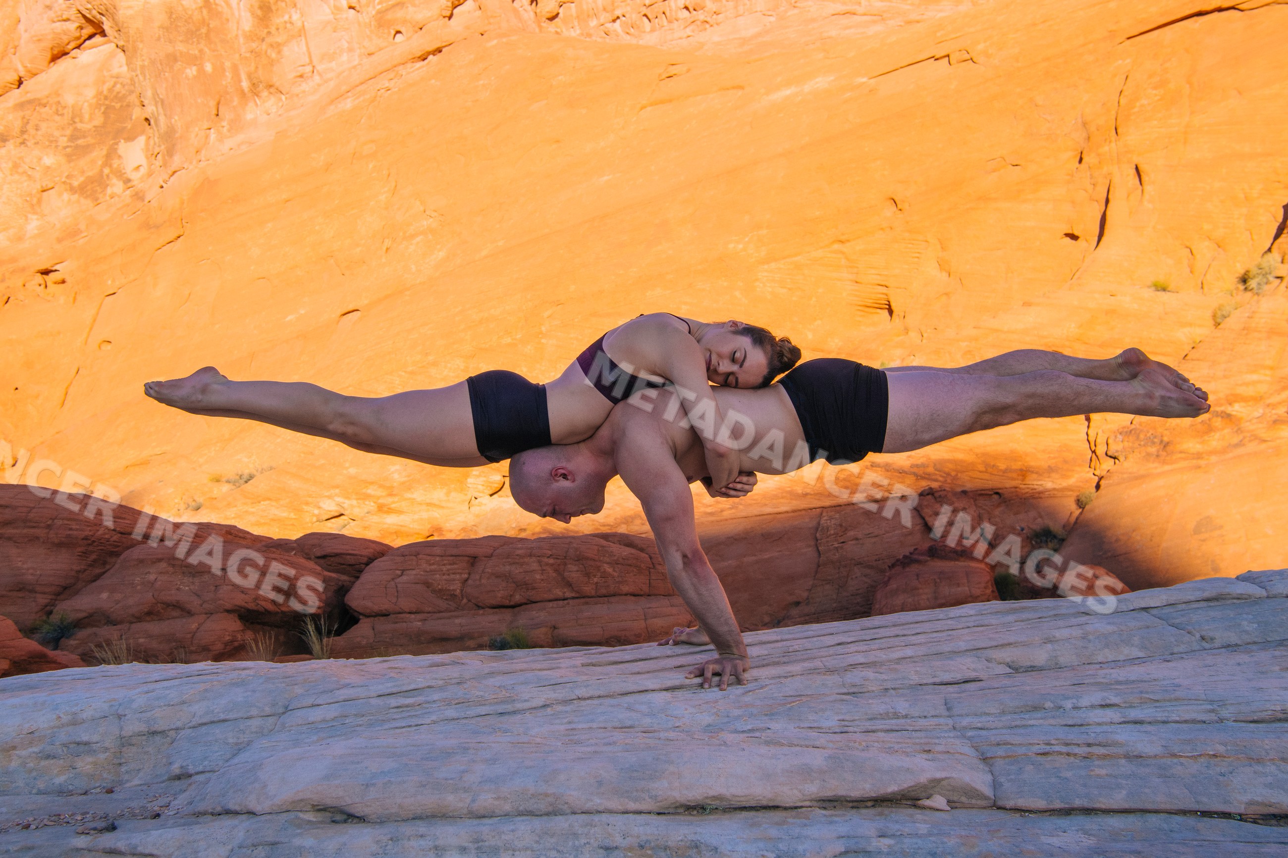 Two white people performing acrobatic yoga balancing pose on desert