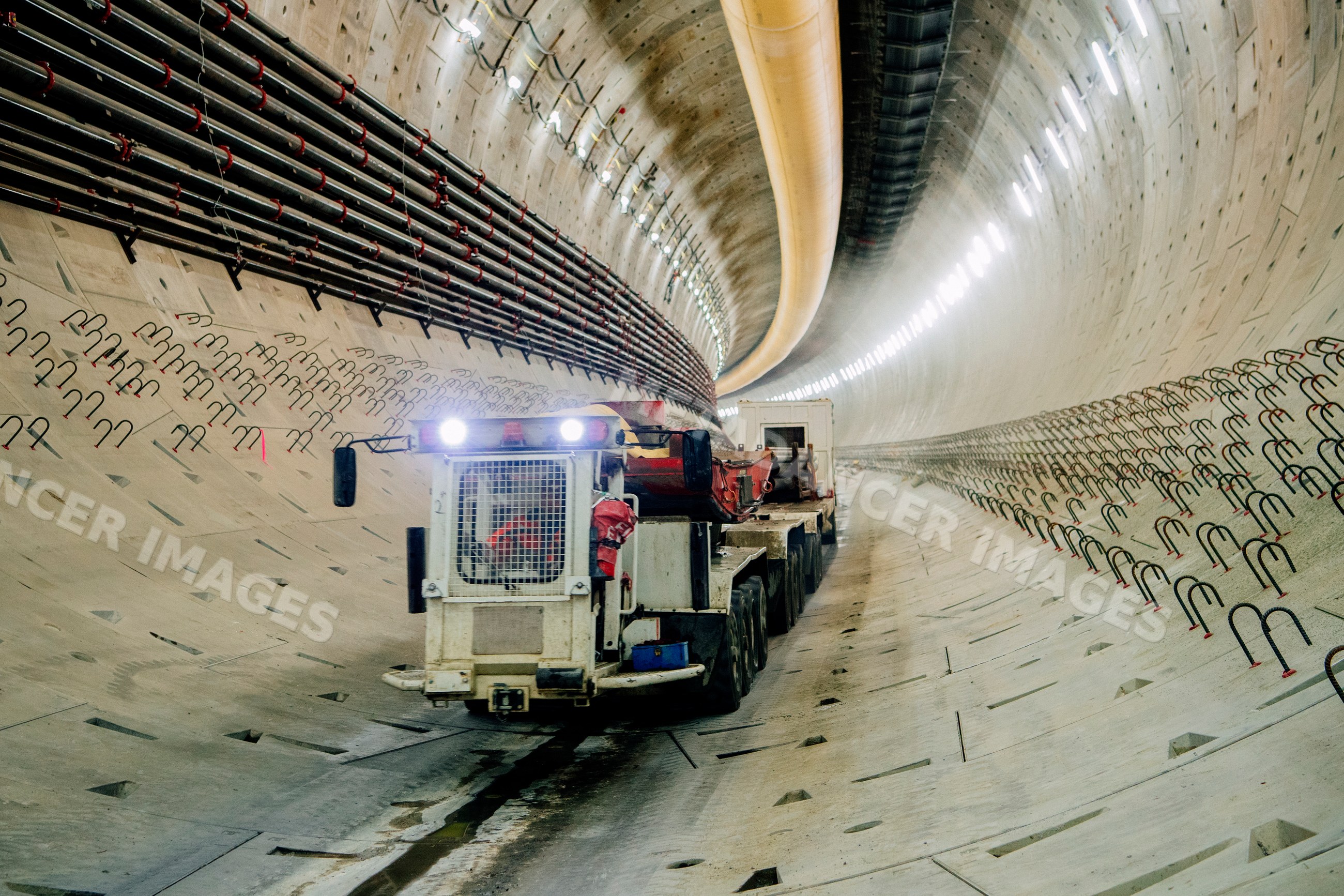 A construction vehicle works inside a large concrete-lined tunnel