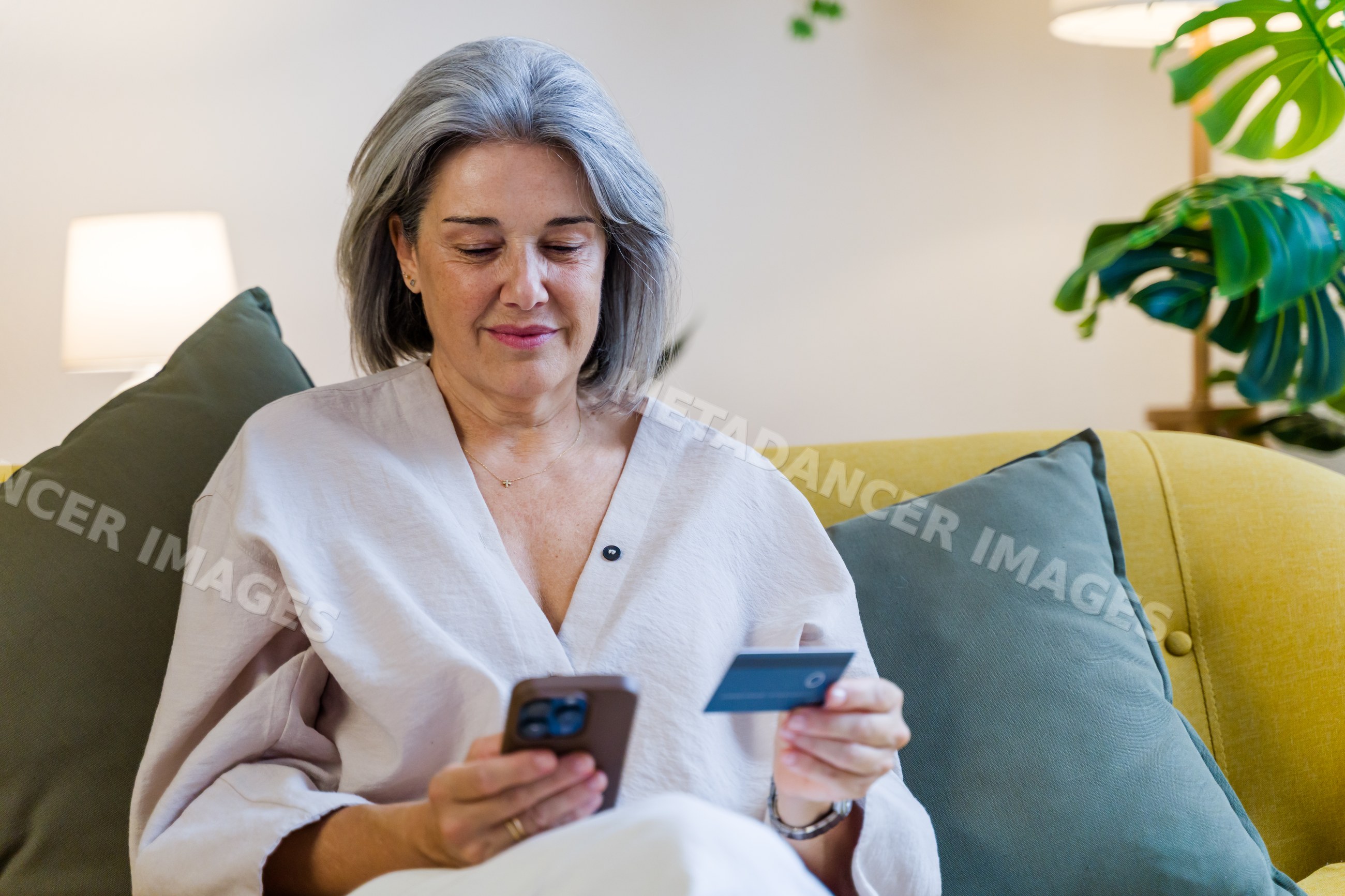 White woman using smartphone and credit card on sofa in living room