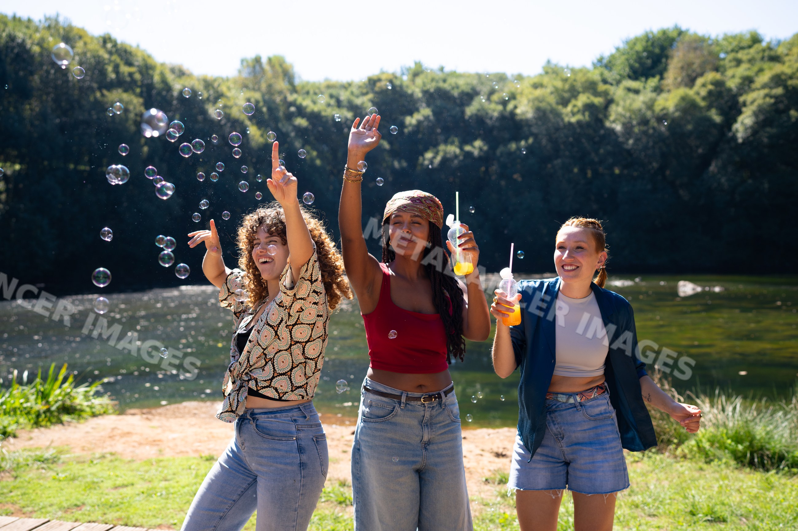 White and African American women playing with bubbles by lake on sunny