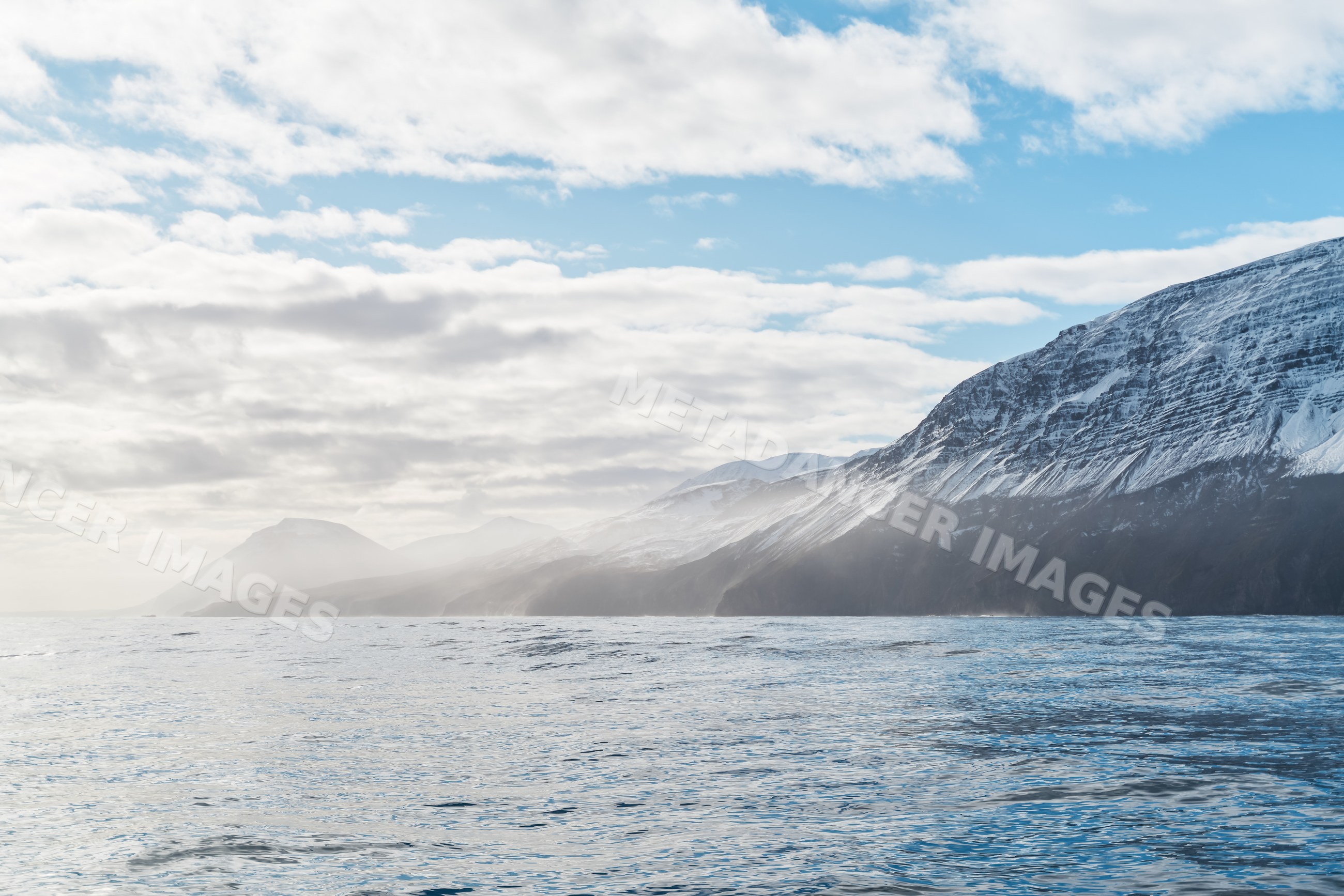 Snowy mountains overlooking the calm sea under a cloudy sky