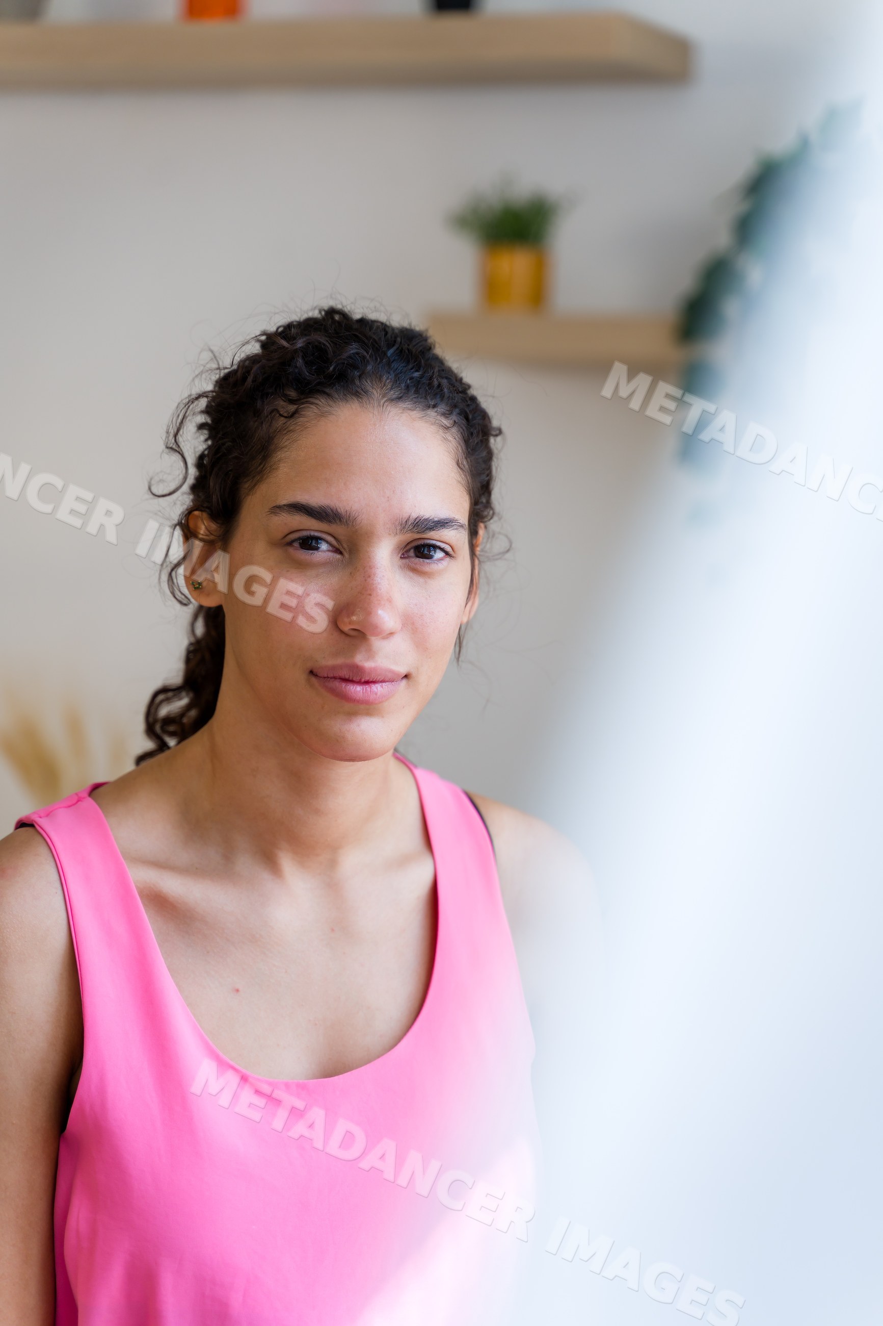 Young Hispanic woman with curly hair wears pink sleeveless top indoors