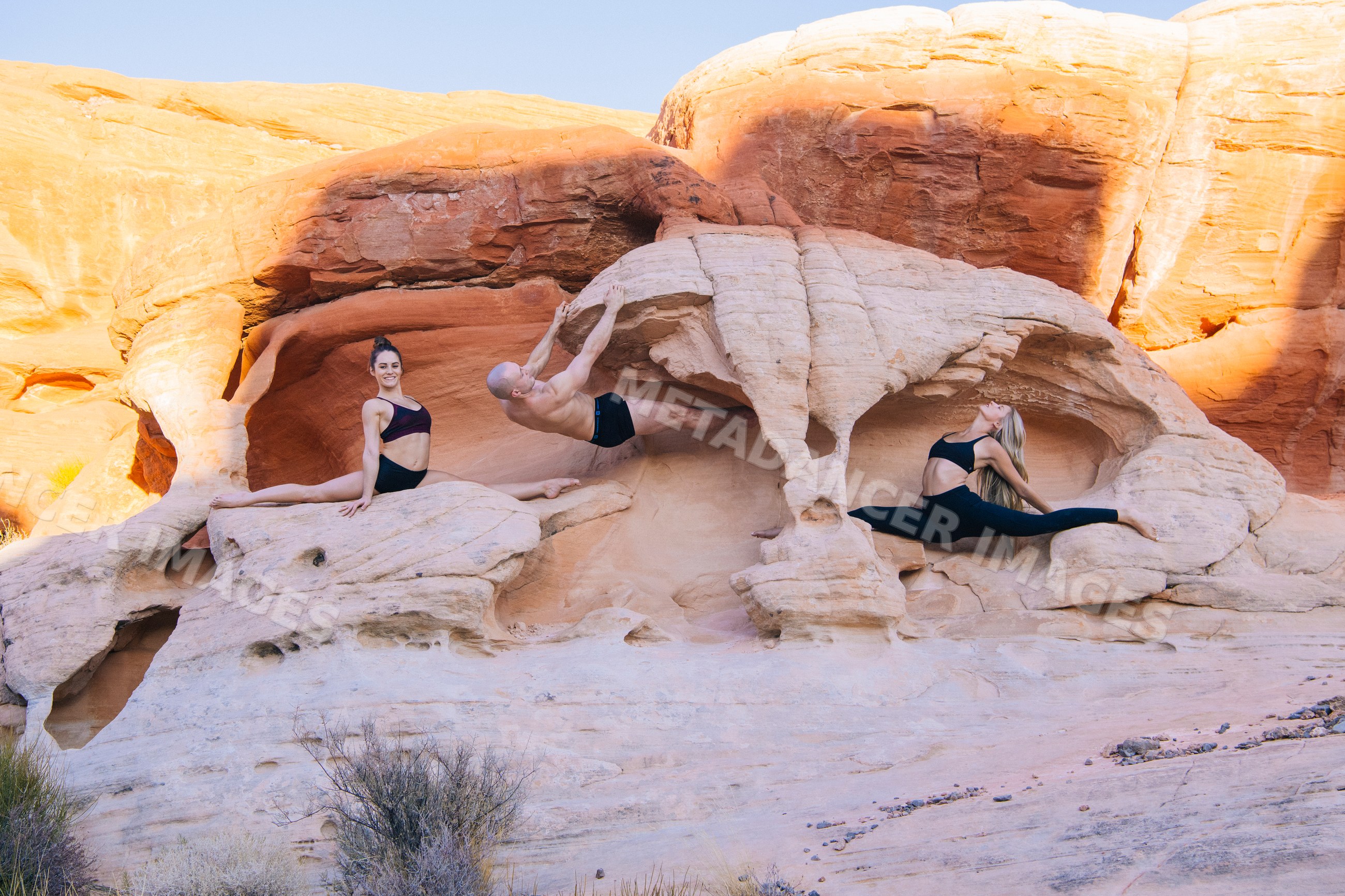 Three white people practicing yoga and acrobatics on desert rock
