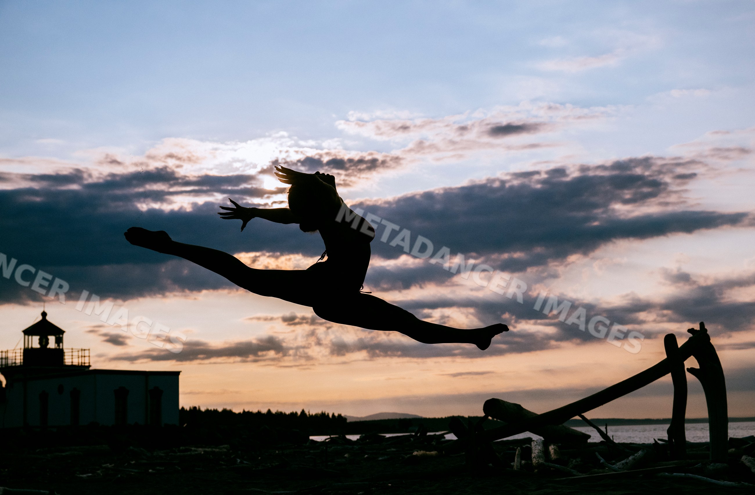 A woman performs a split leap silhouette on a beach