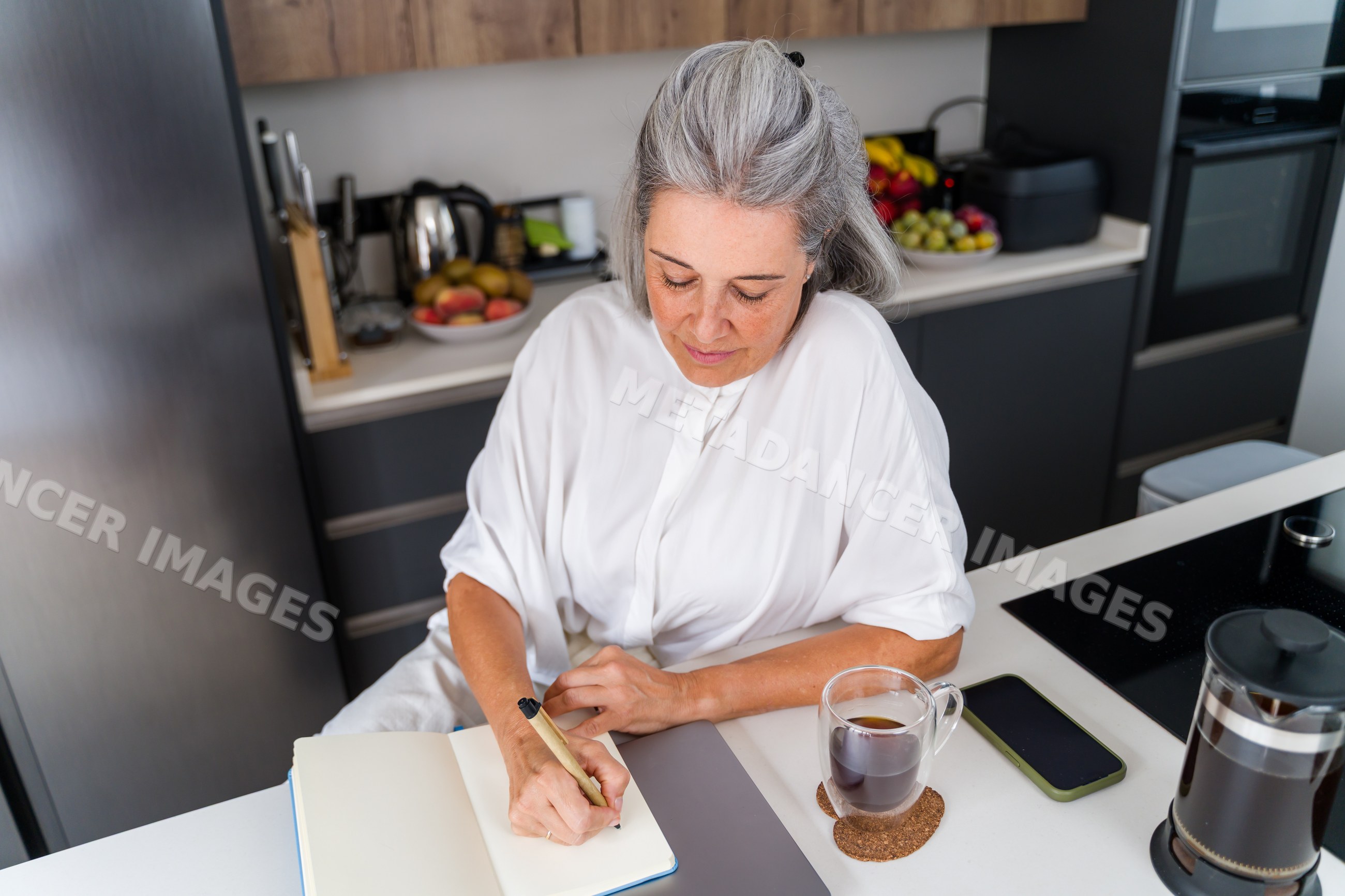 White Woman writing at kitchen counter with coffee and smartphone