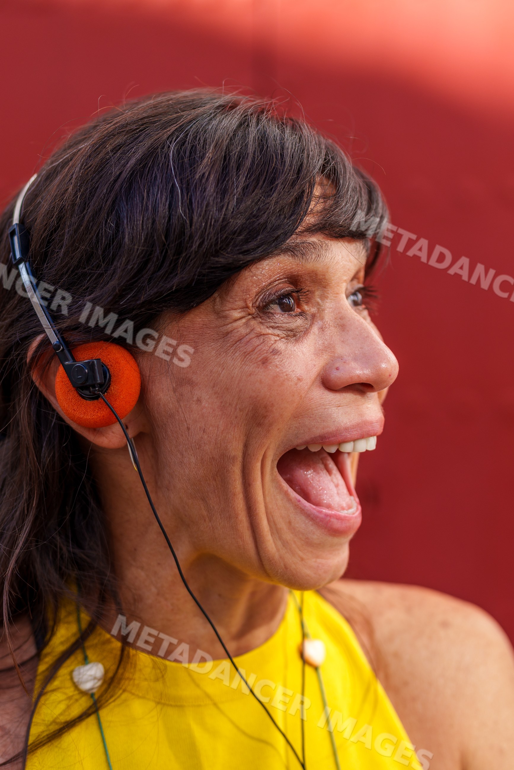 Hispanic woman wearing orange headphones speaking against red
