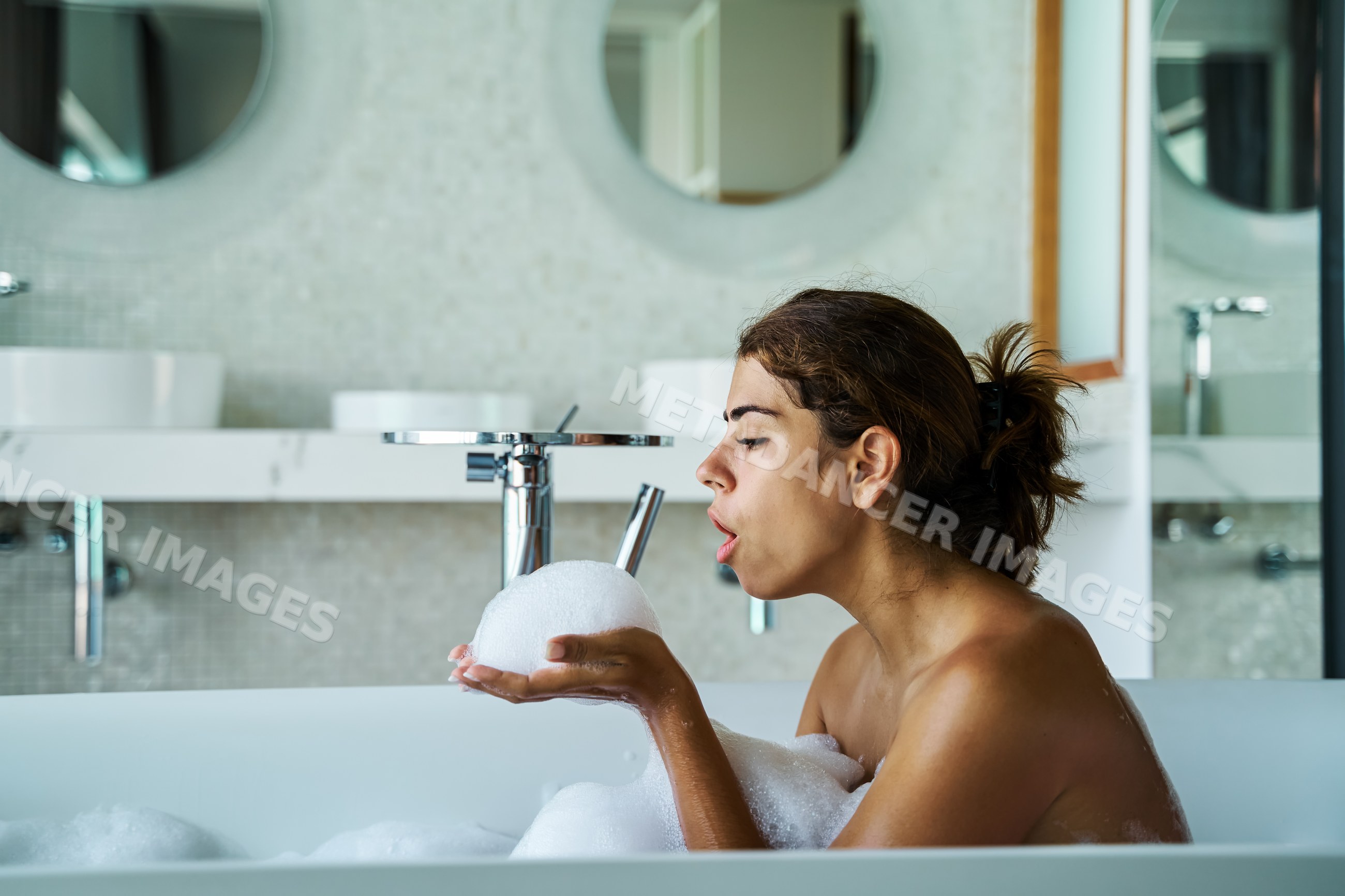 A white woman enjoys a bubble bath in a modern bathroom