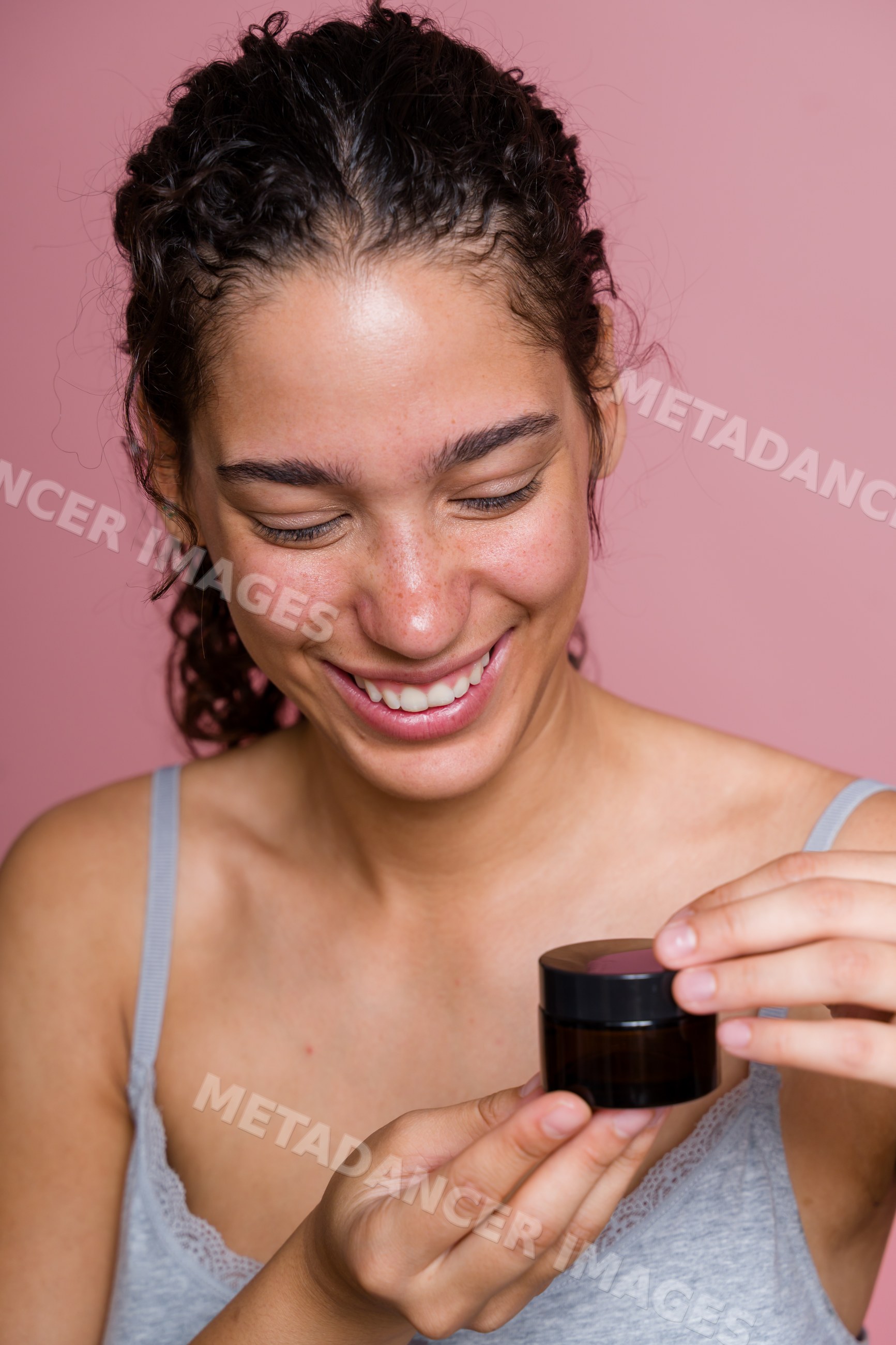 Hispanic woman smiling while holding a skincare jar in beauty shoot