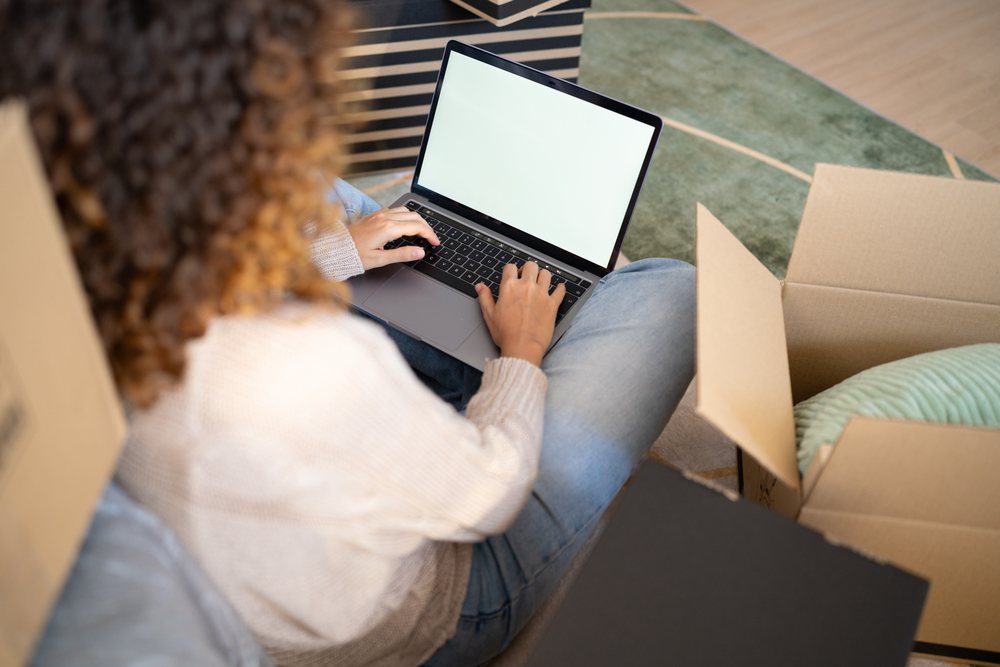 White woman typing on laptop during moving with cardboard boxes