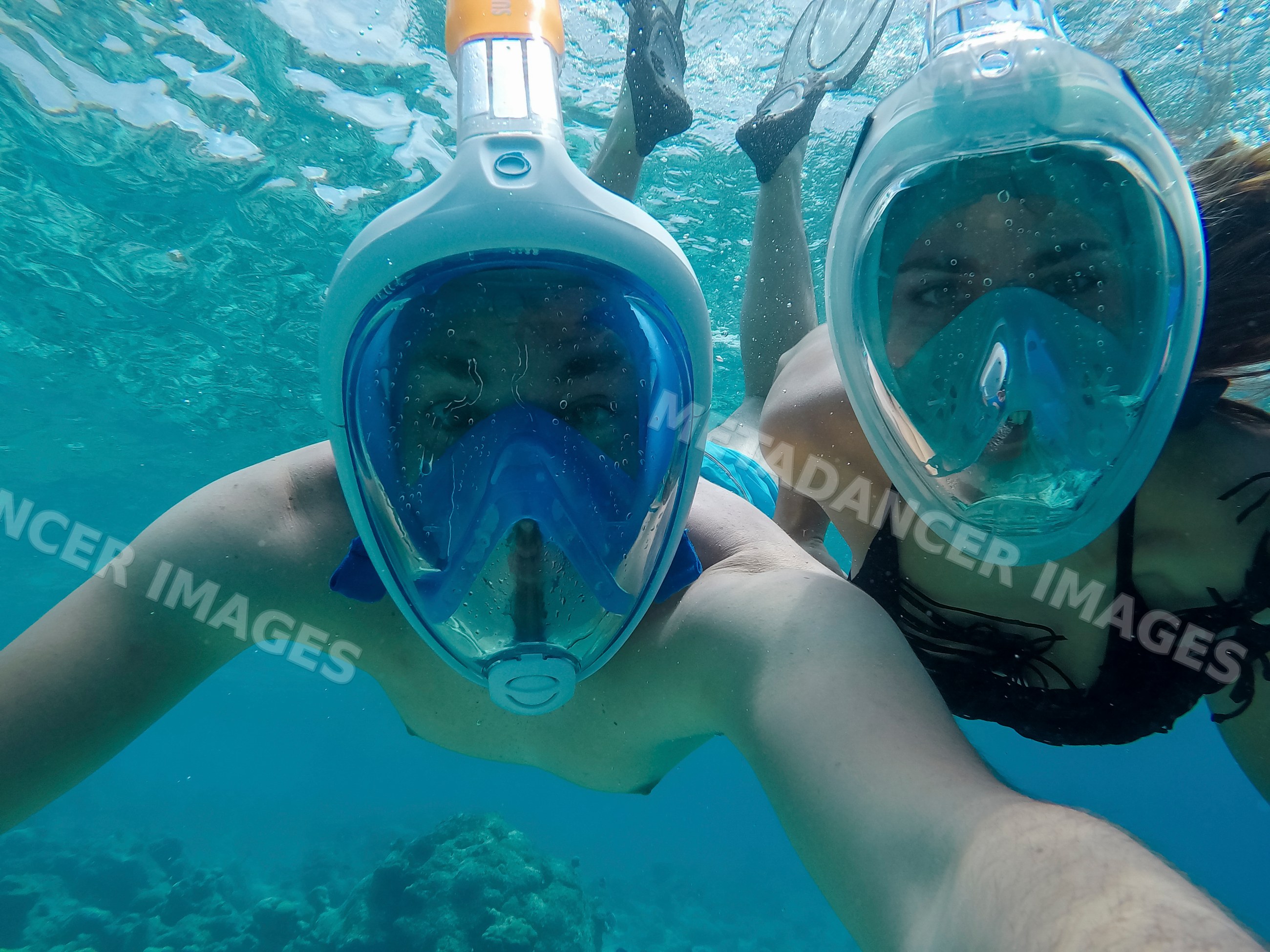 A couple snorkeling underwater with full face masks