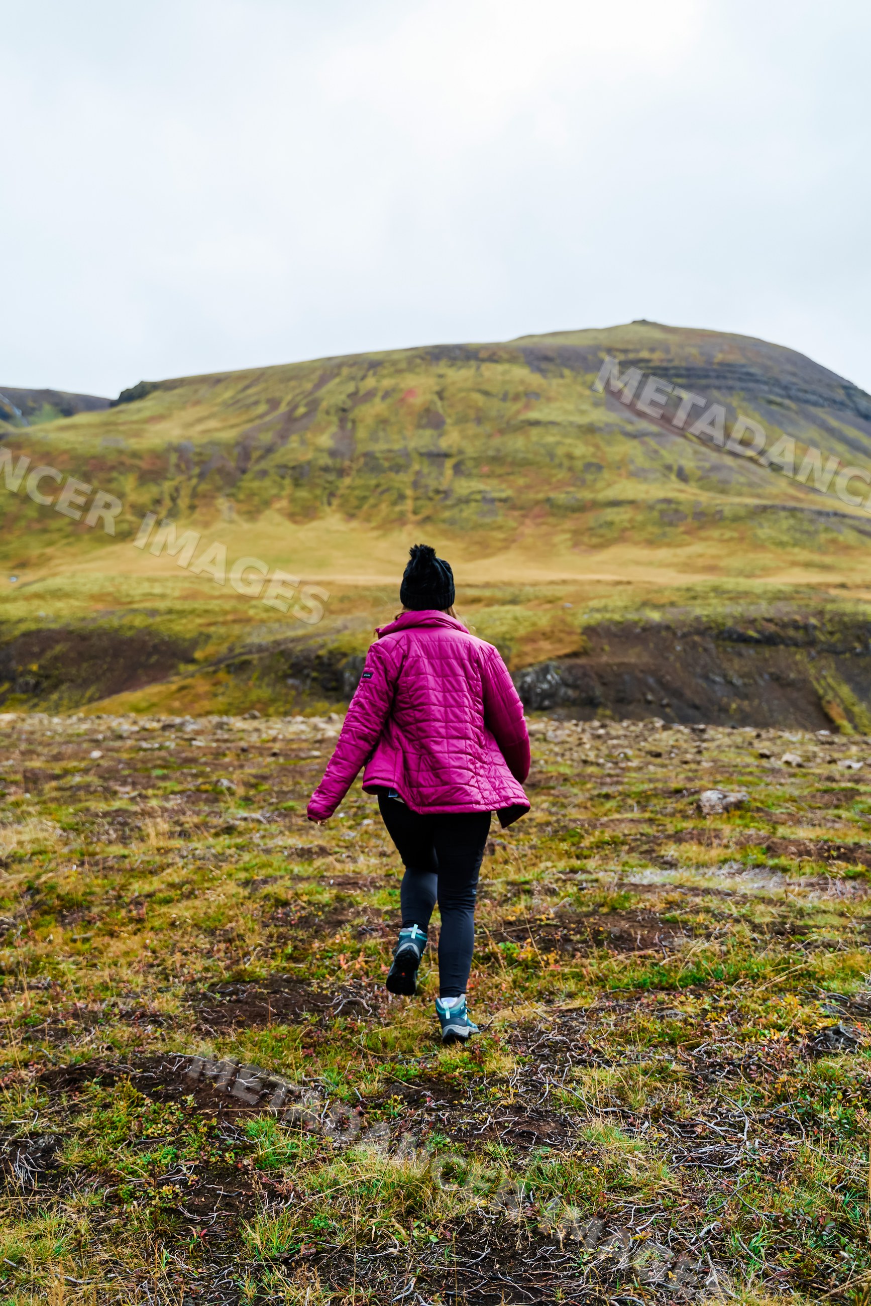A white person hikes through a grassy mountain landscape