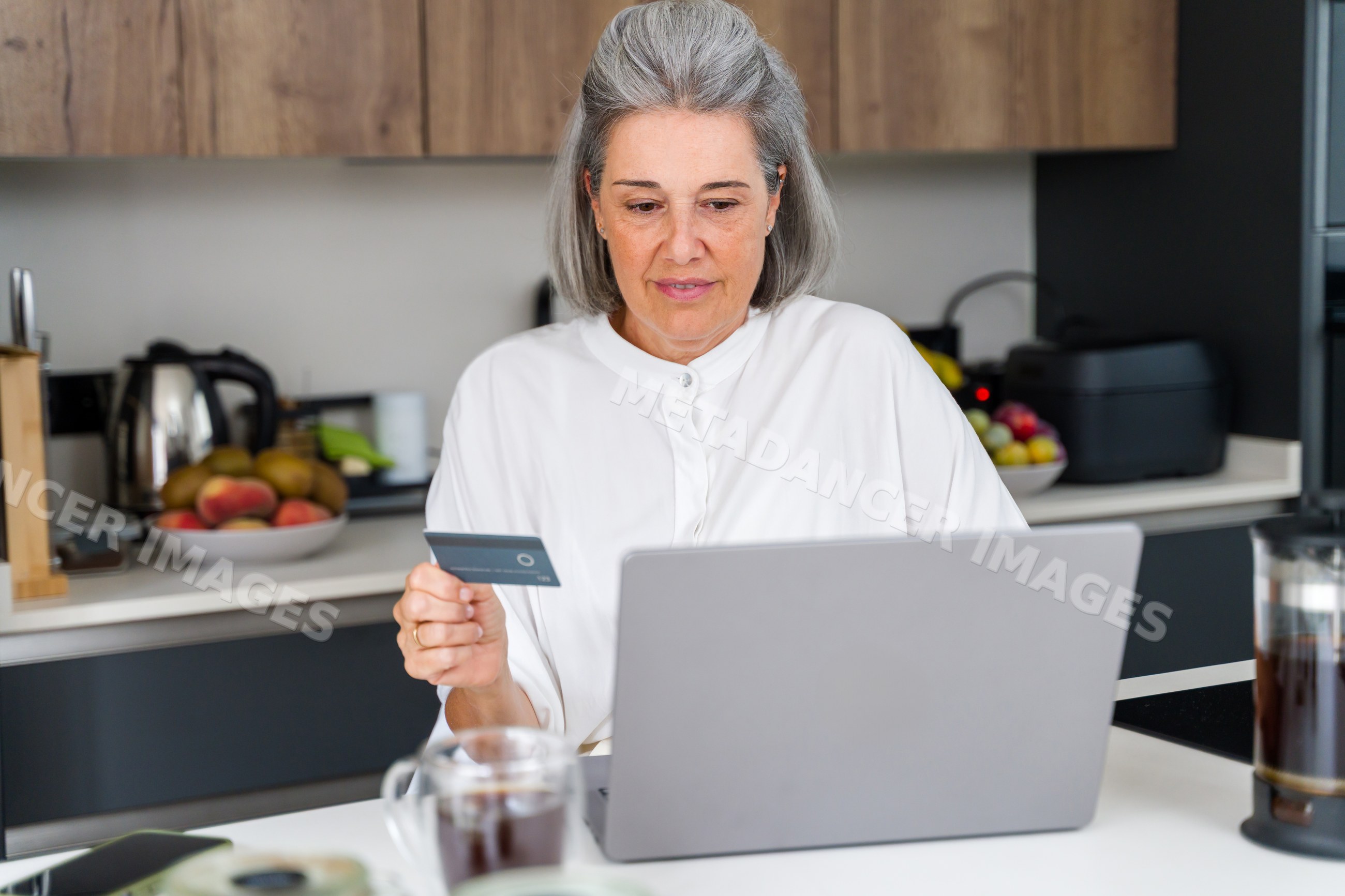 White Woman shopping online on laptop at kitchen table in Spain
