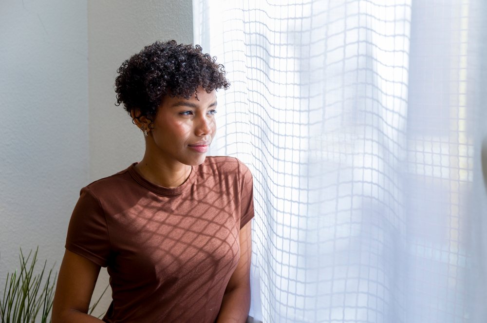 Young African American woman looking out window at home
