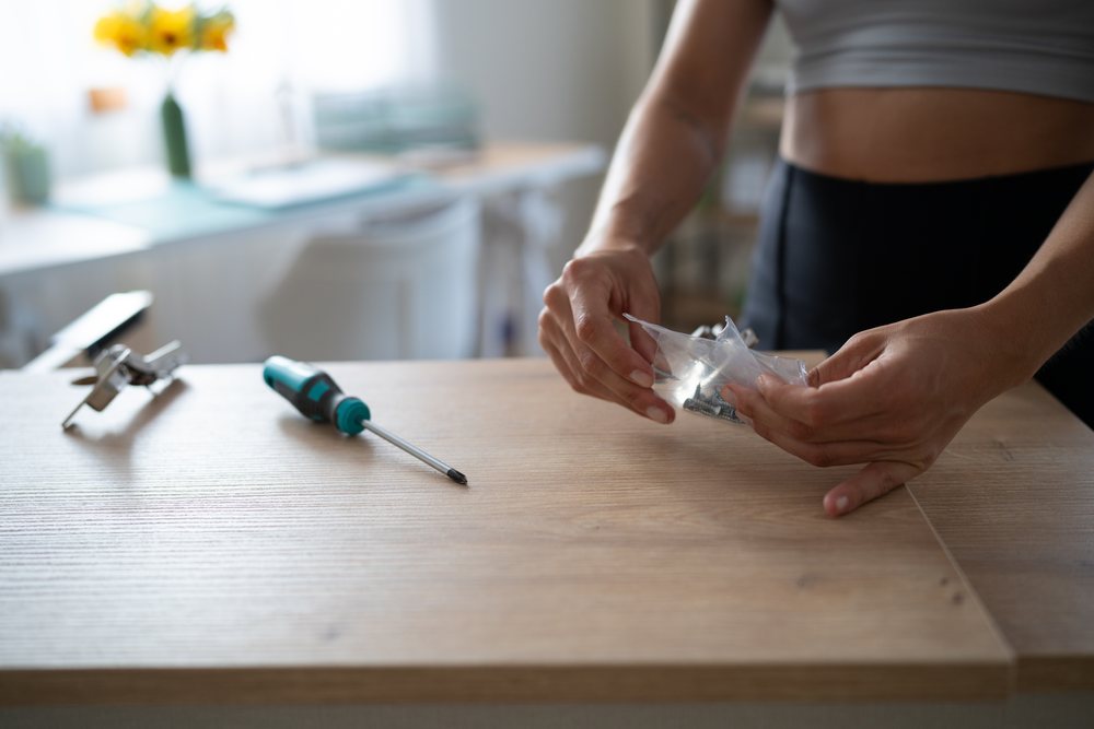 A white person assembling wooden furniture by unpacking screws