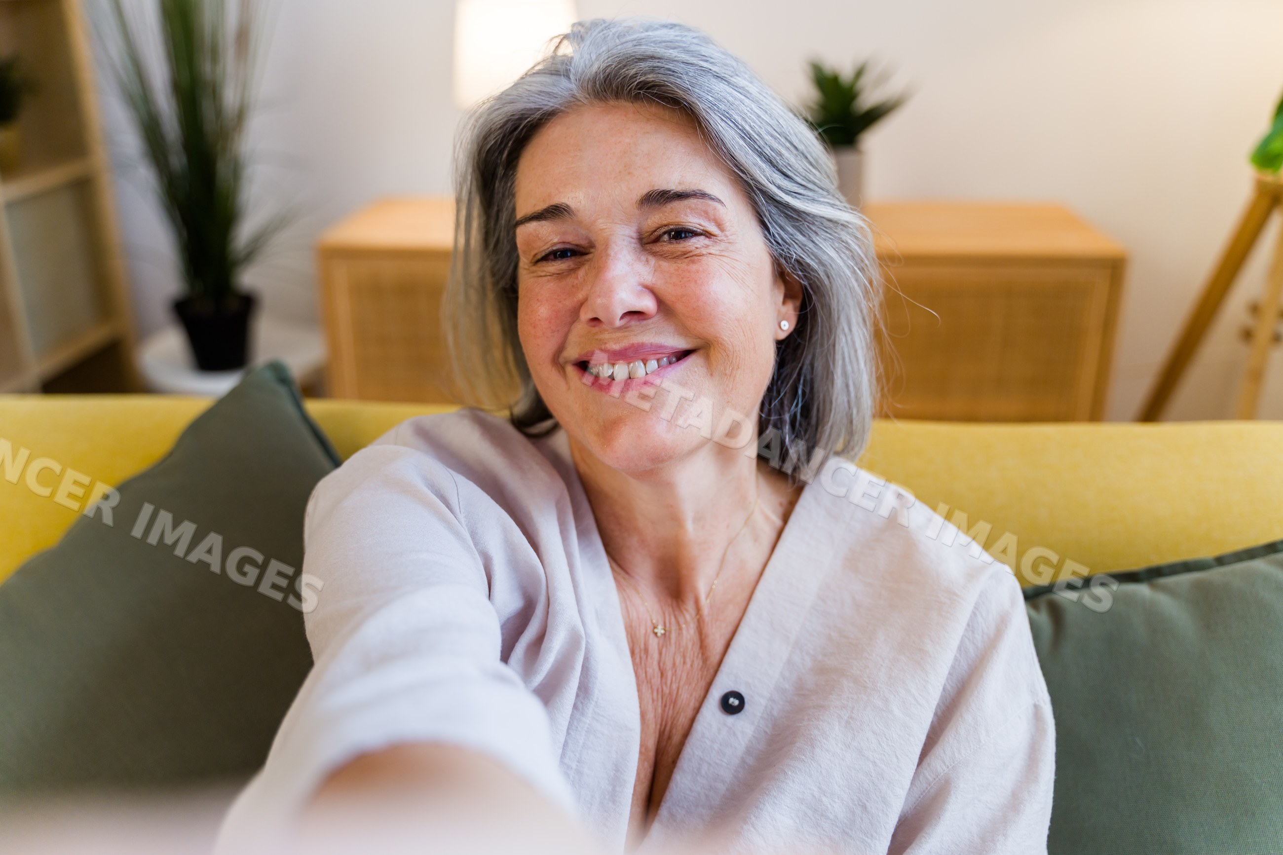 Middle-aged white woman smiling taking selfie on couch indoors