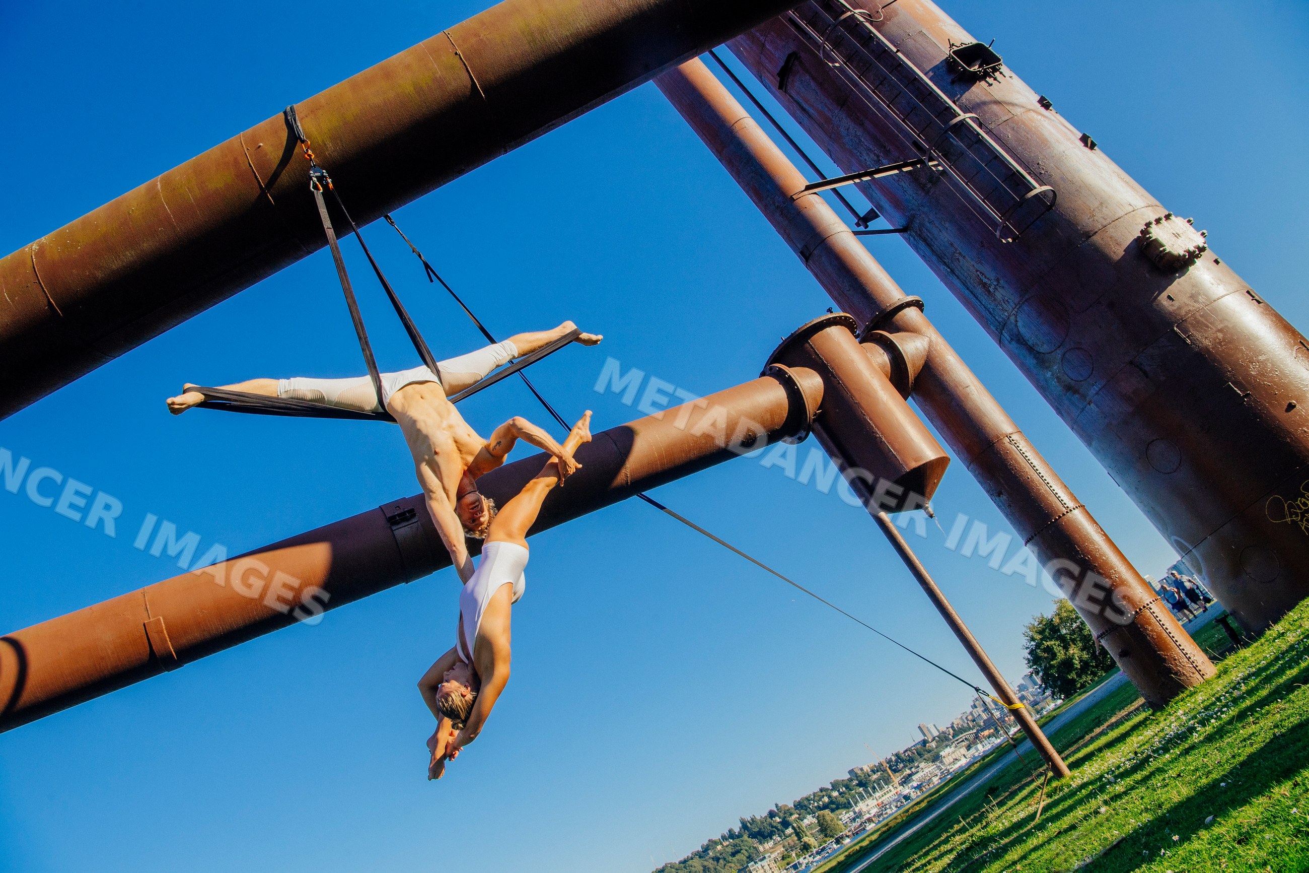 Aerialists performing acrobatics with aerial silks on industrial pipes