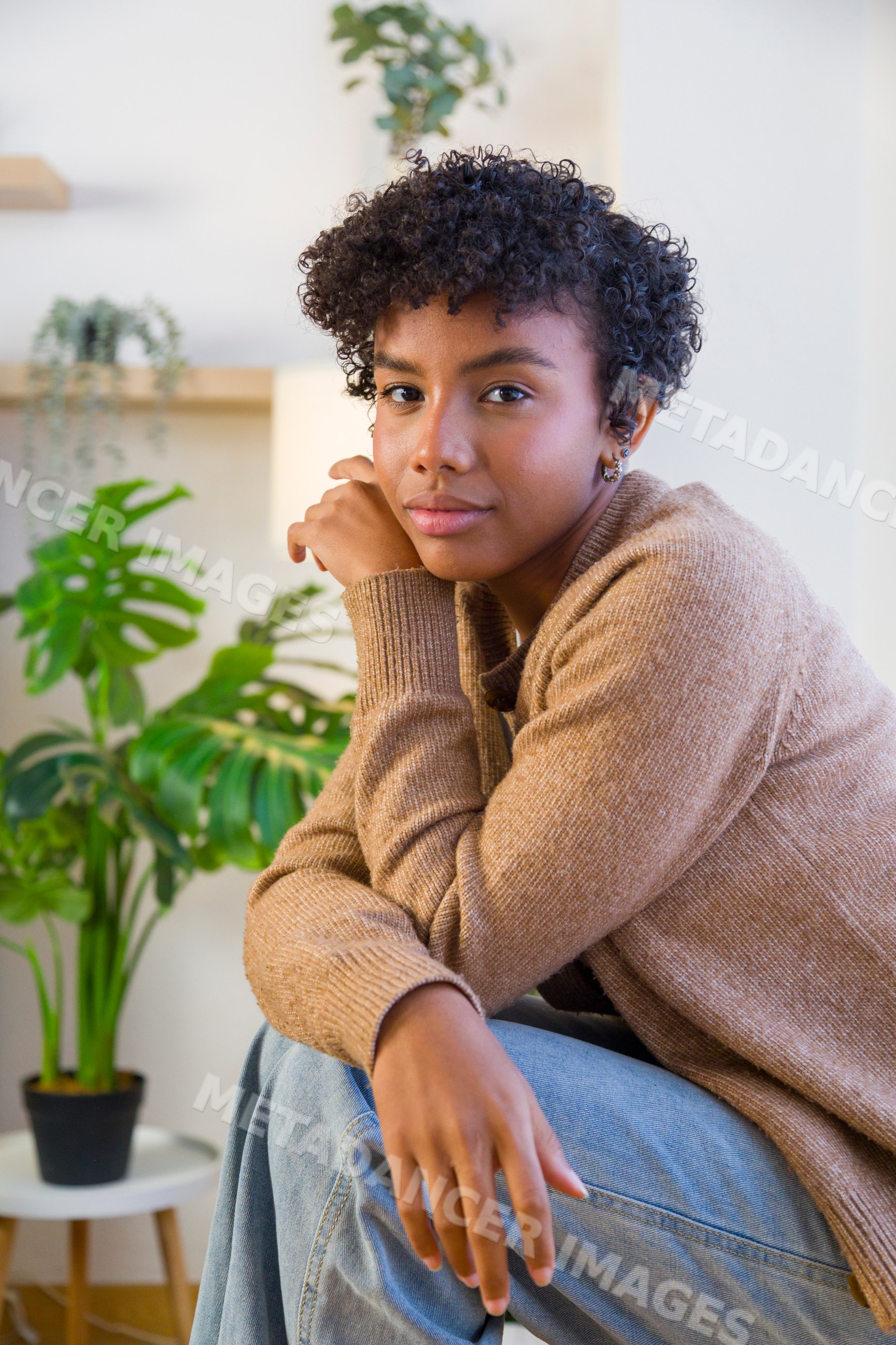 Young African American woman posing indoors by a monstera plant