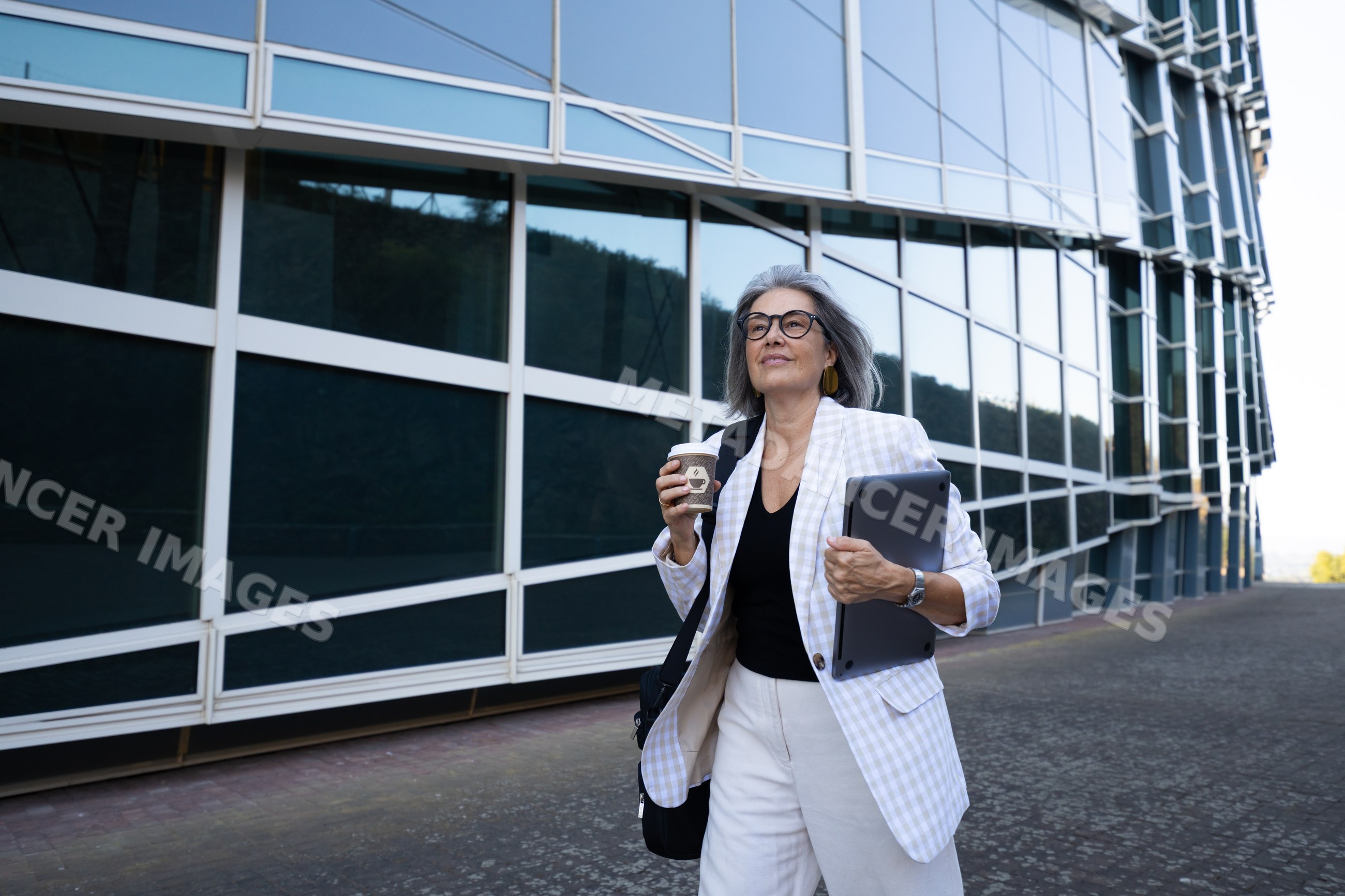 Businesswoman walking outside modern building with coffee and tablet