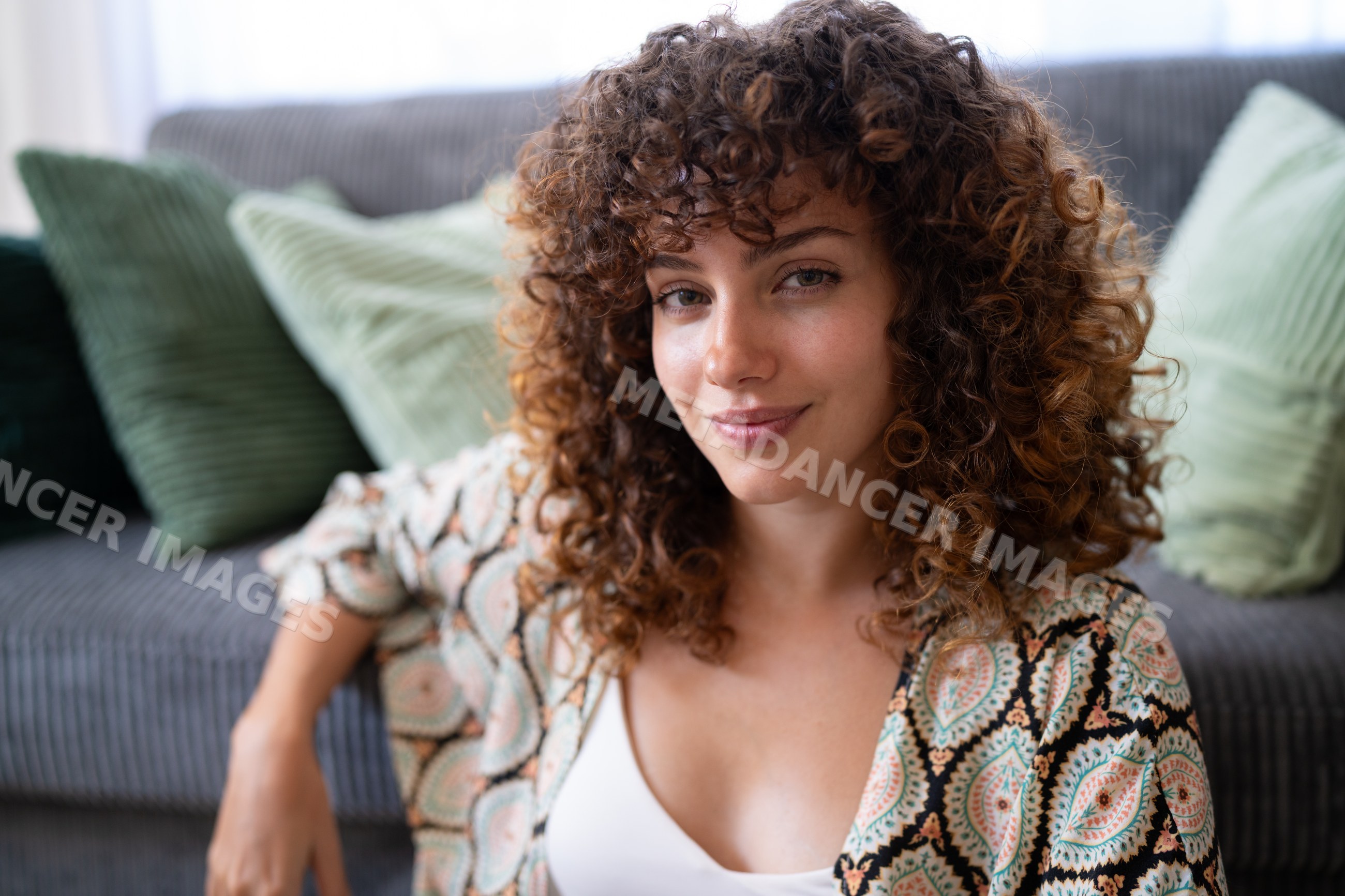 White woman with curly hair smiling while seated on sofa