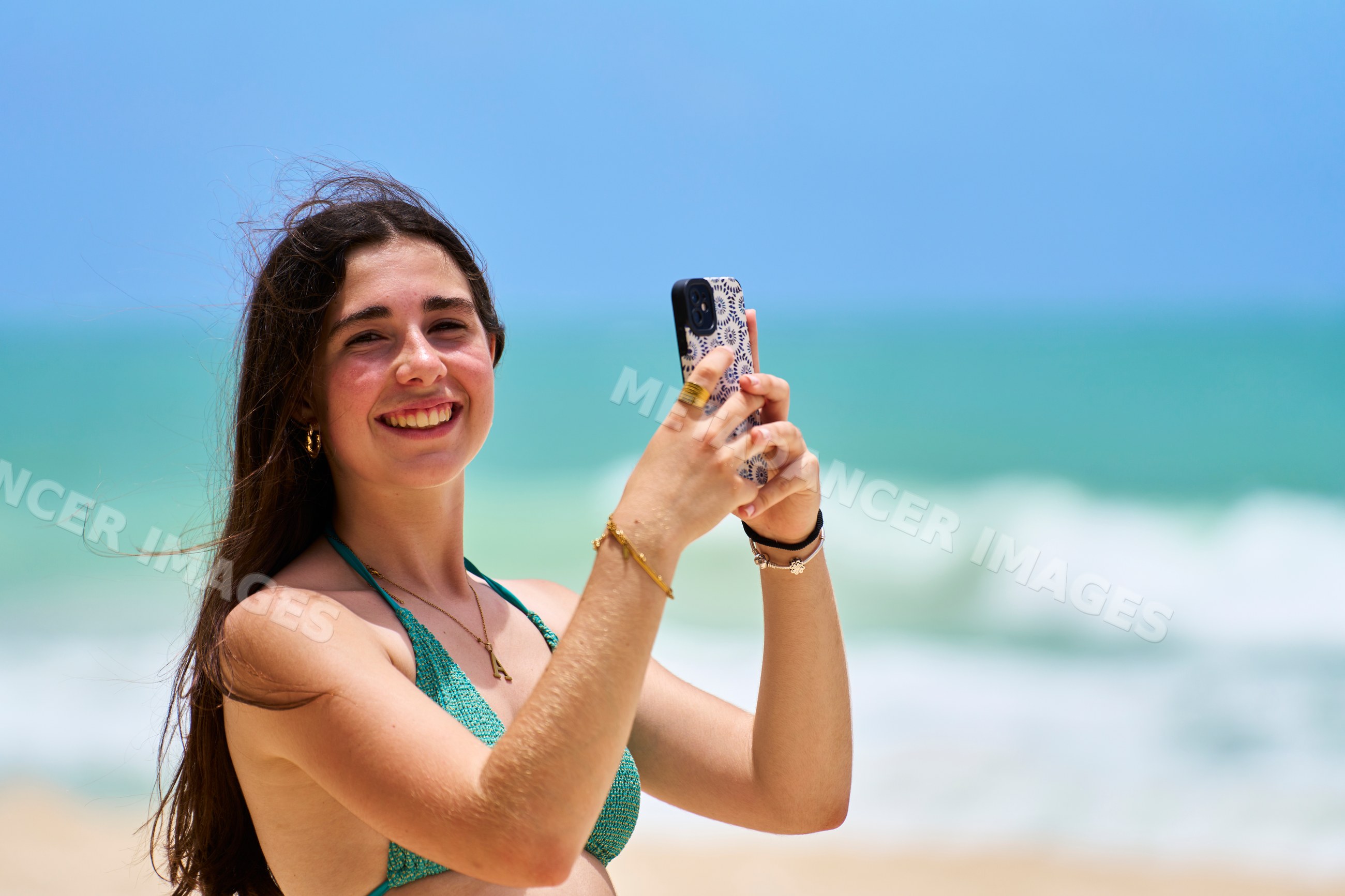 White woman taking photo on beach with ocean waves