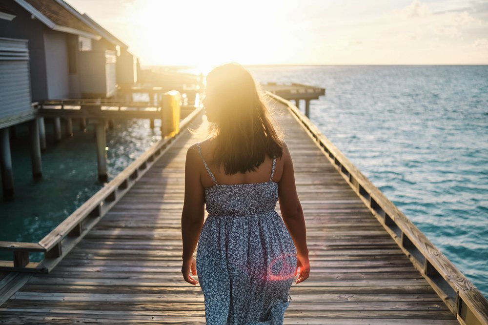 A white woman walking on a wooden pier at sunset in the Maldives