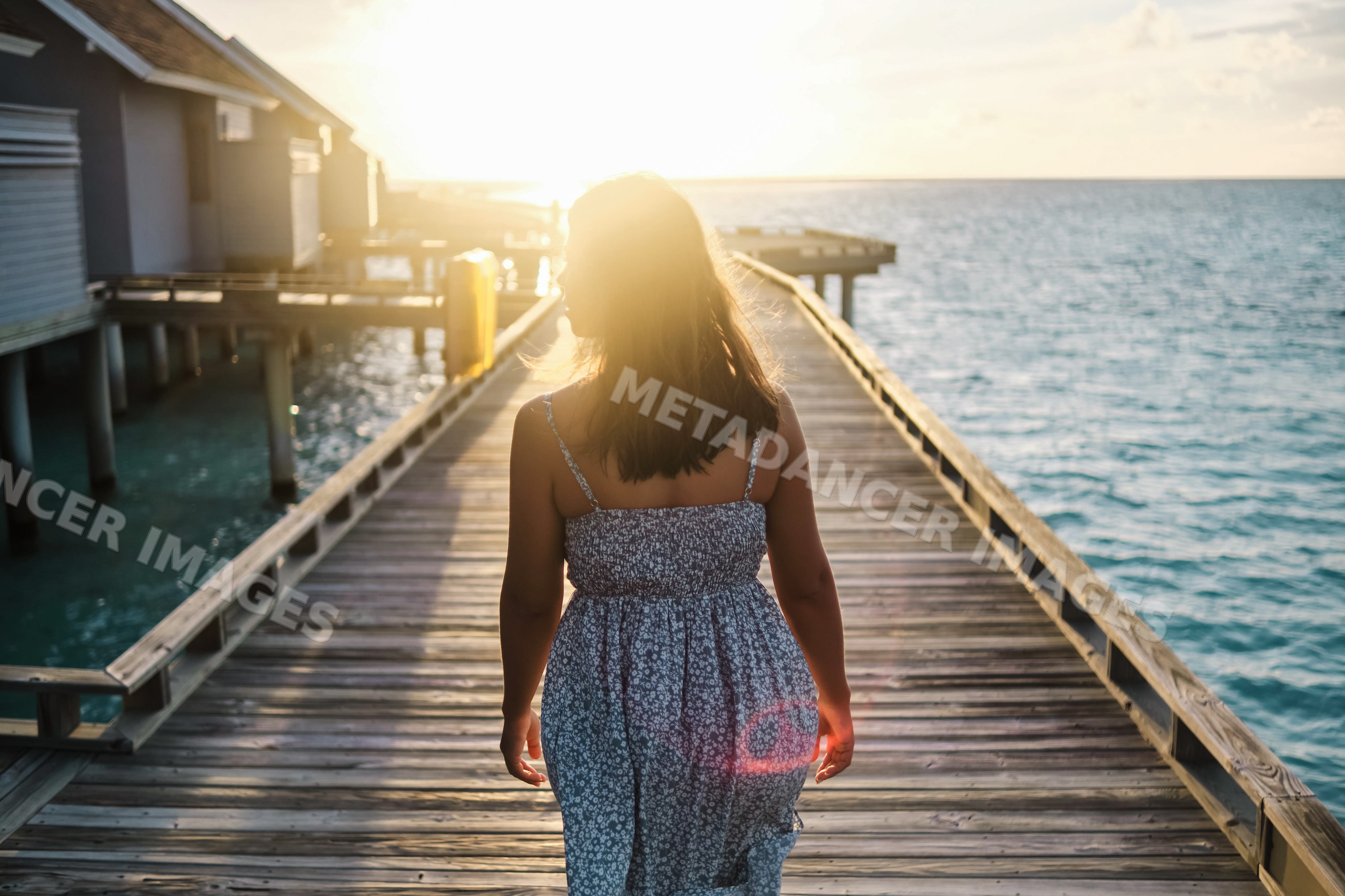 A white woman walking on a wooden pier at sunset in the Maldives