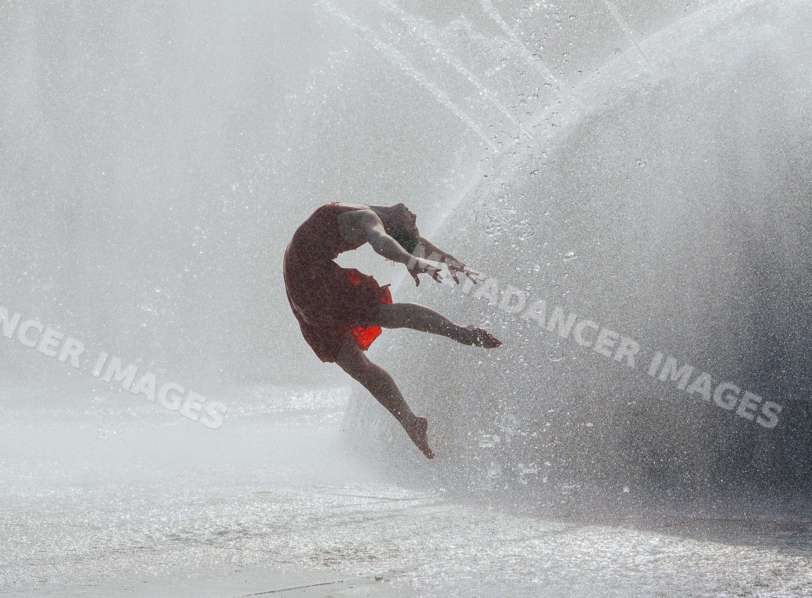 White woman jumping through water splash in red dress outdoors