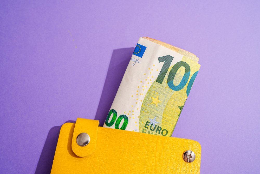 Yellow wallet with rolled euro notes on purple studio background