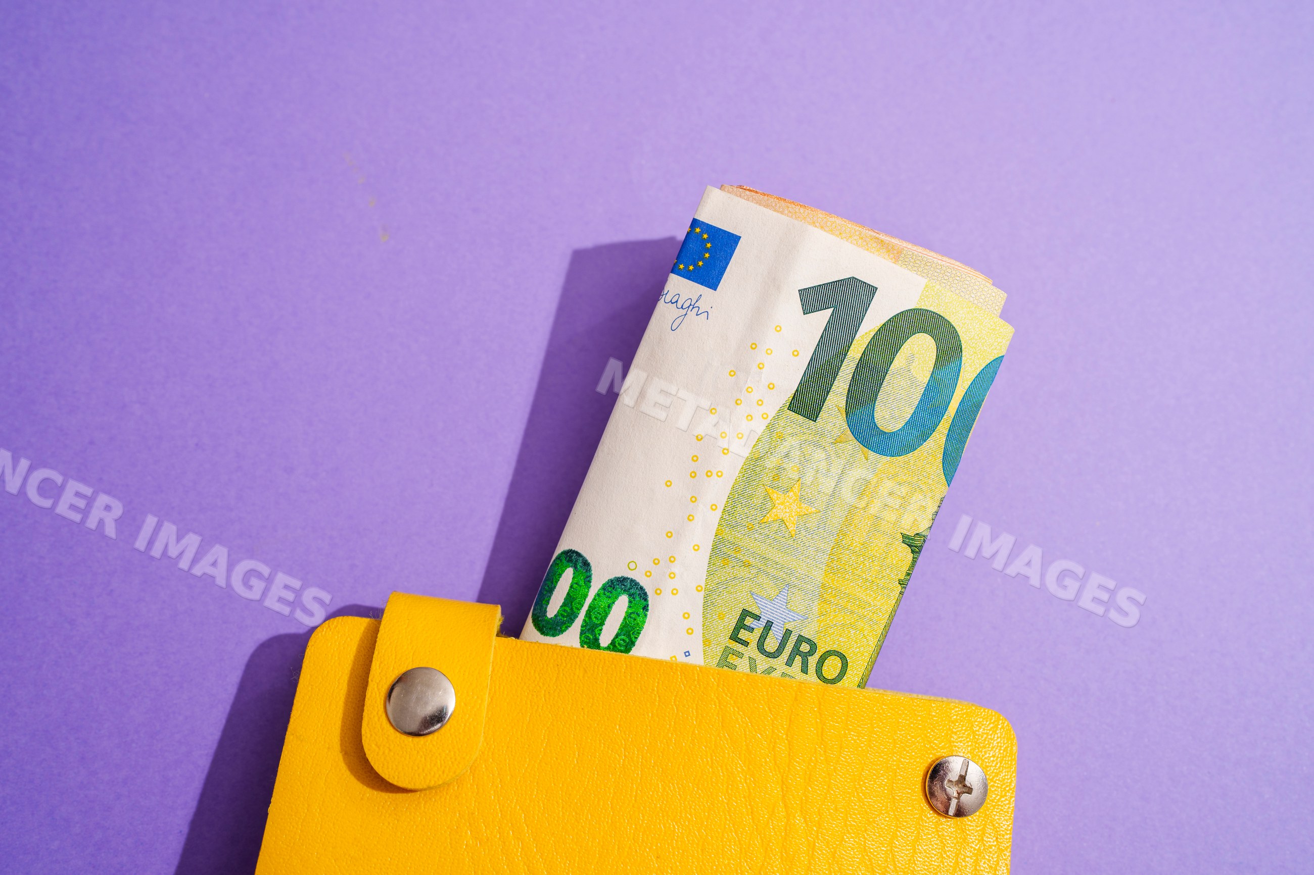 Yellow wallet with rolled euro notes on purple studio background