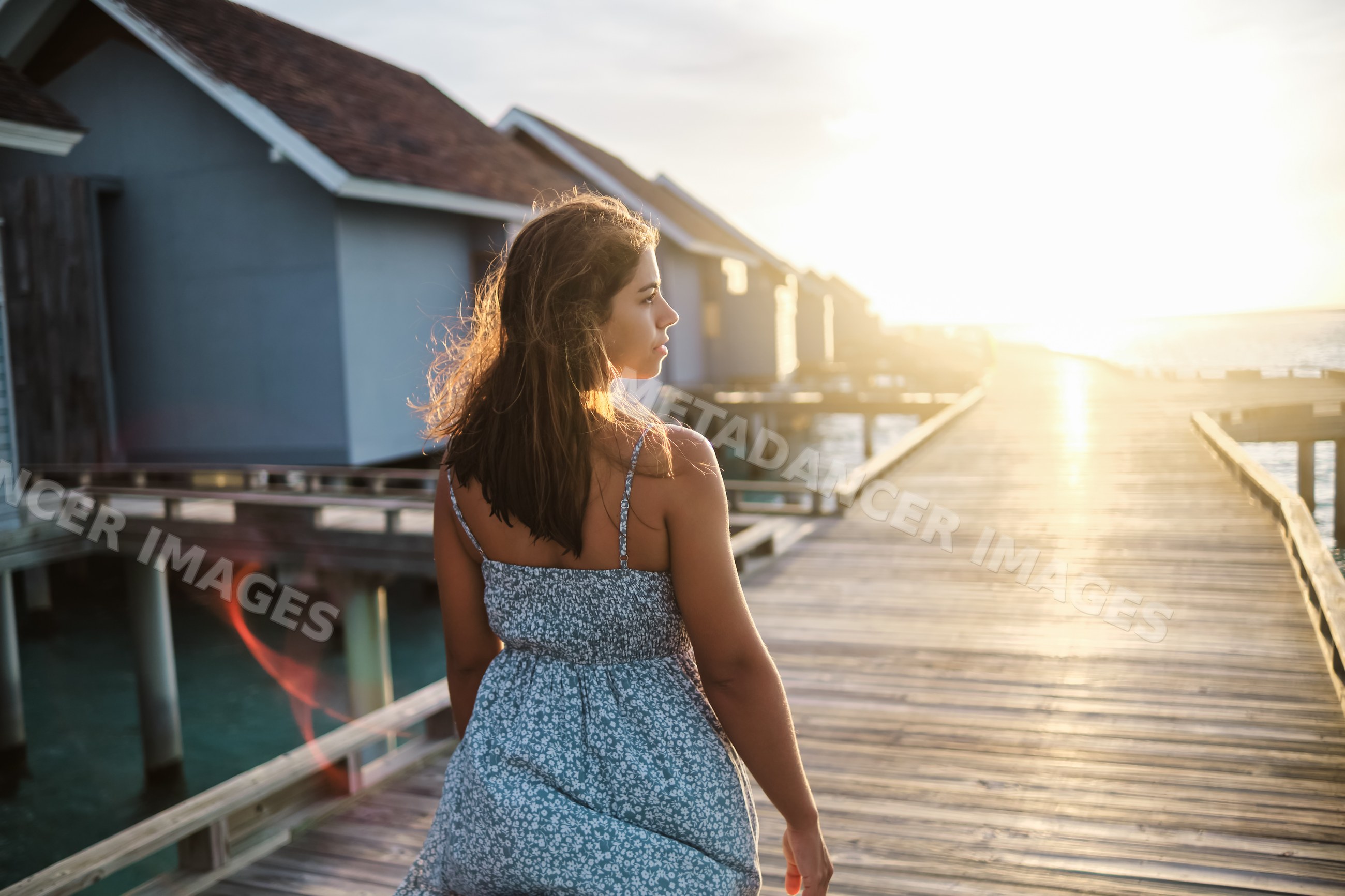A white woman walks along a boardwalk by overwater bungalows
