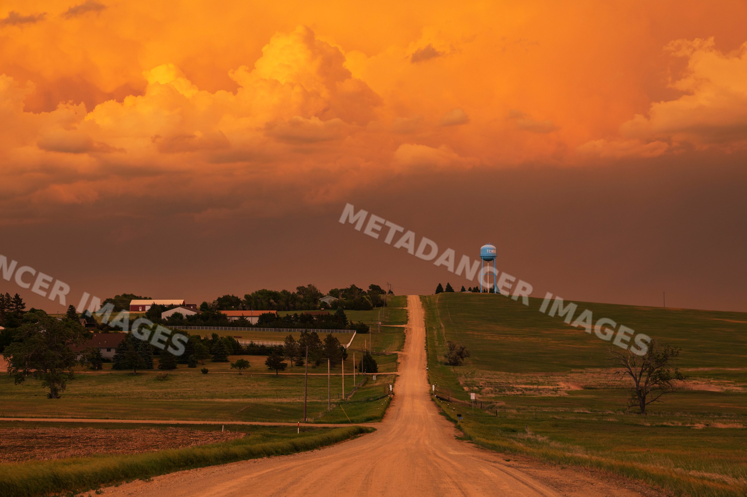 Dirt Road and water tower near winner under stormy sky