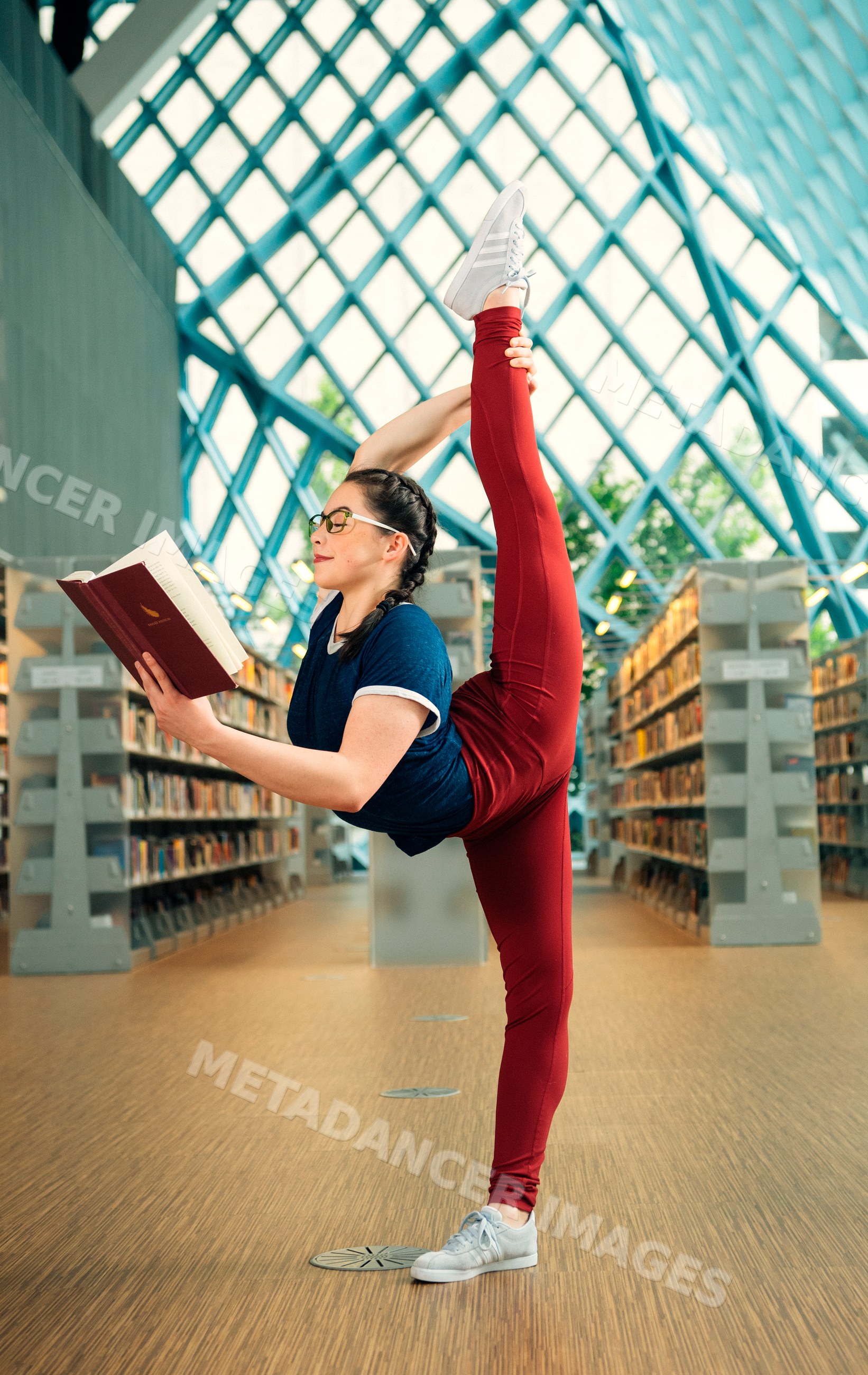 A young woman does a yoga stretch while reading a book
