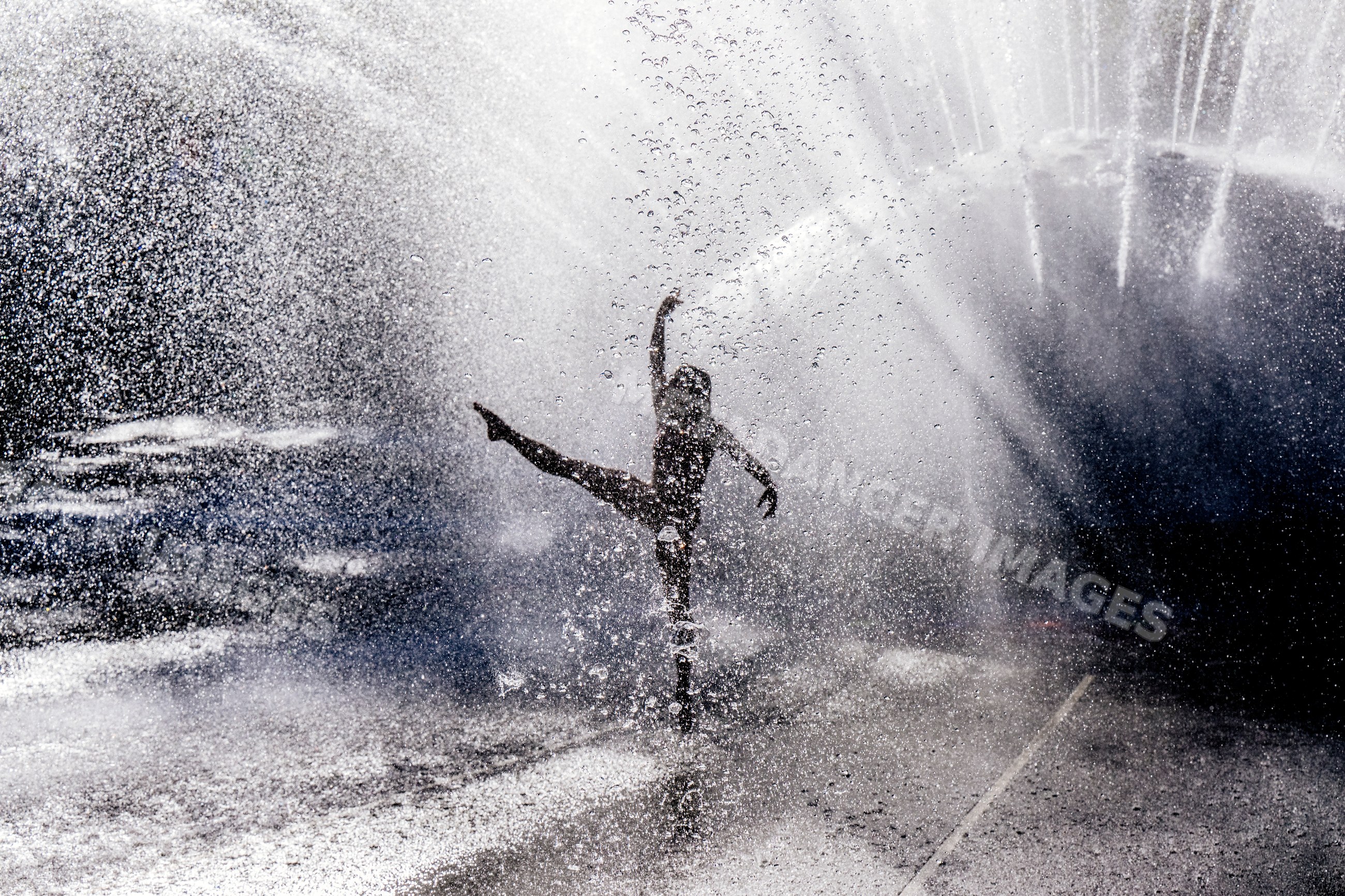 White dancer performing acrobatic yoga pose under water spray