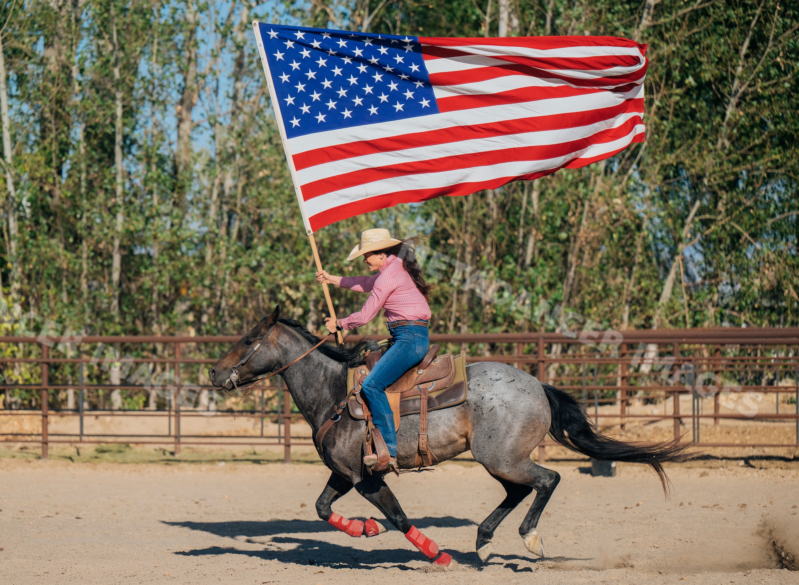 White woman riding horse while carrying american flag in outdoor arena