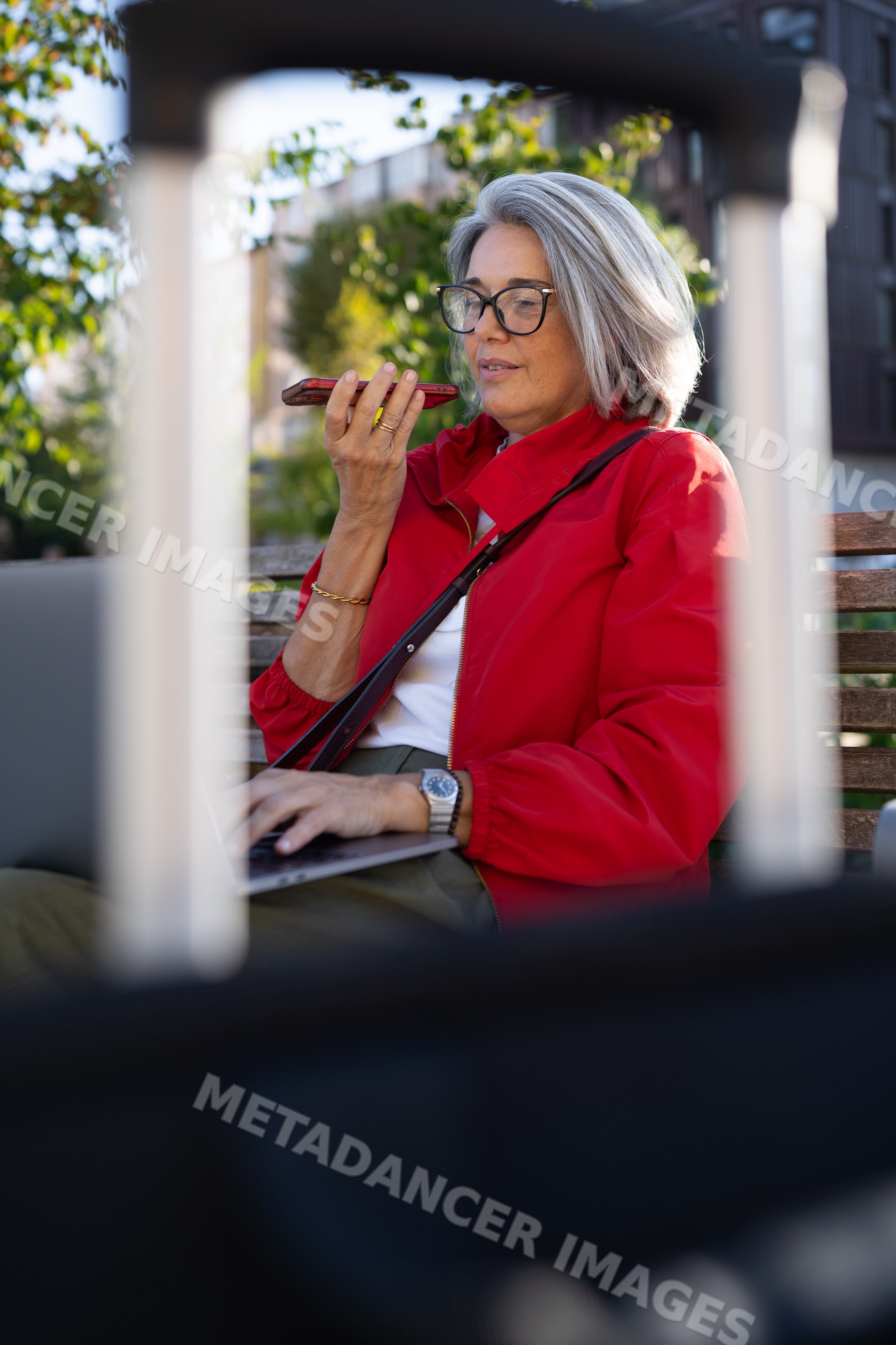White woman using smartphone and laptop outdoors on a bench
