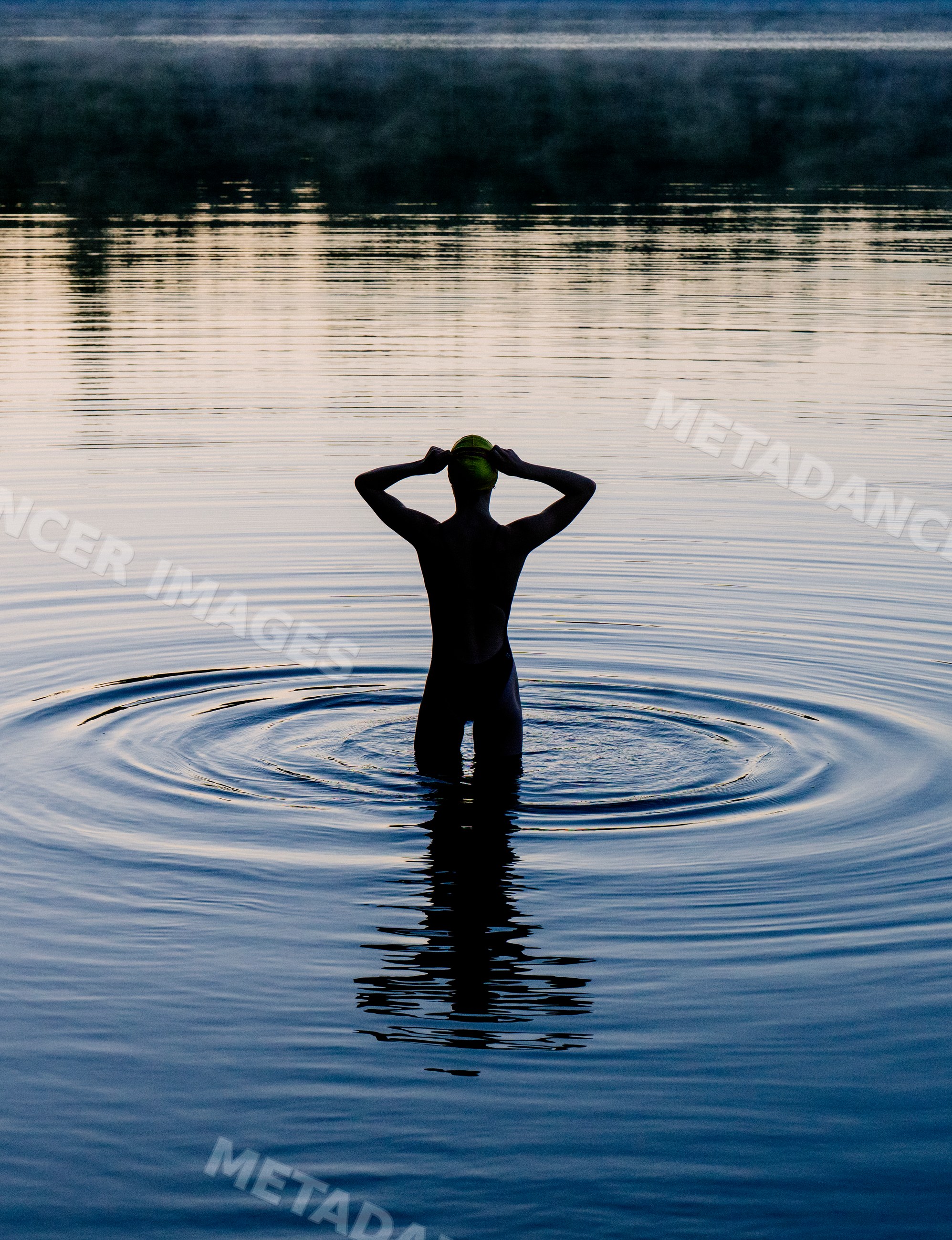 White woman standing in calm lake water at sunset creating ripples