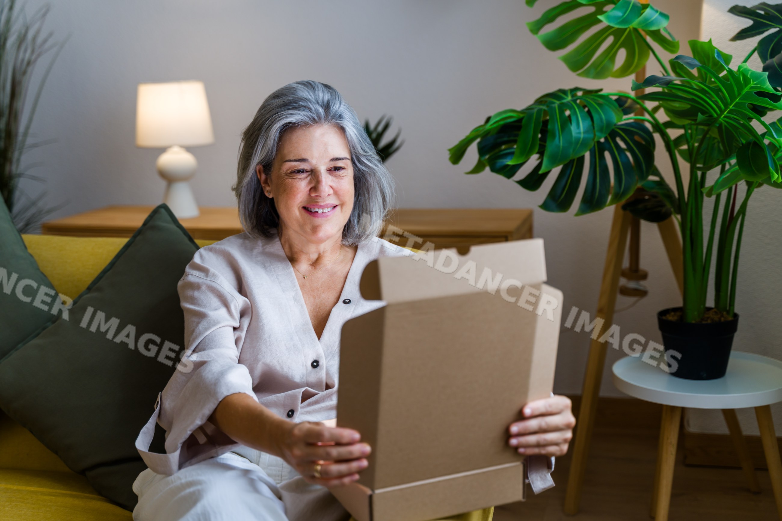 White woman opening cardboard box sitting on sofa in living room