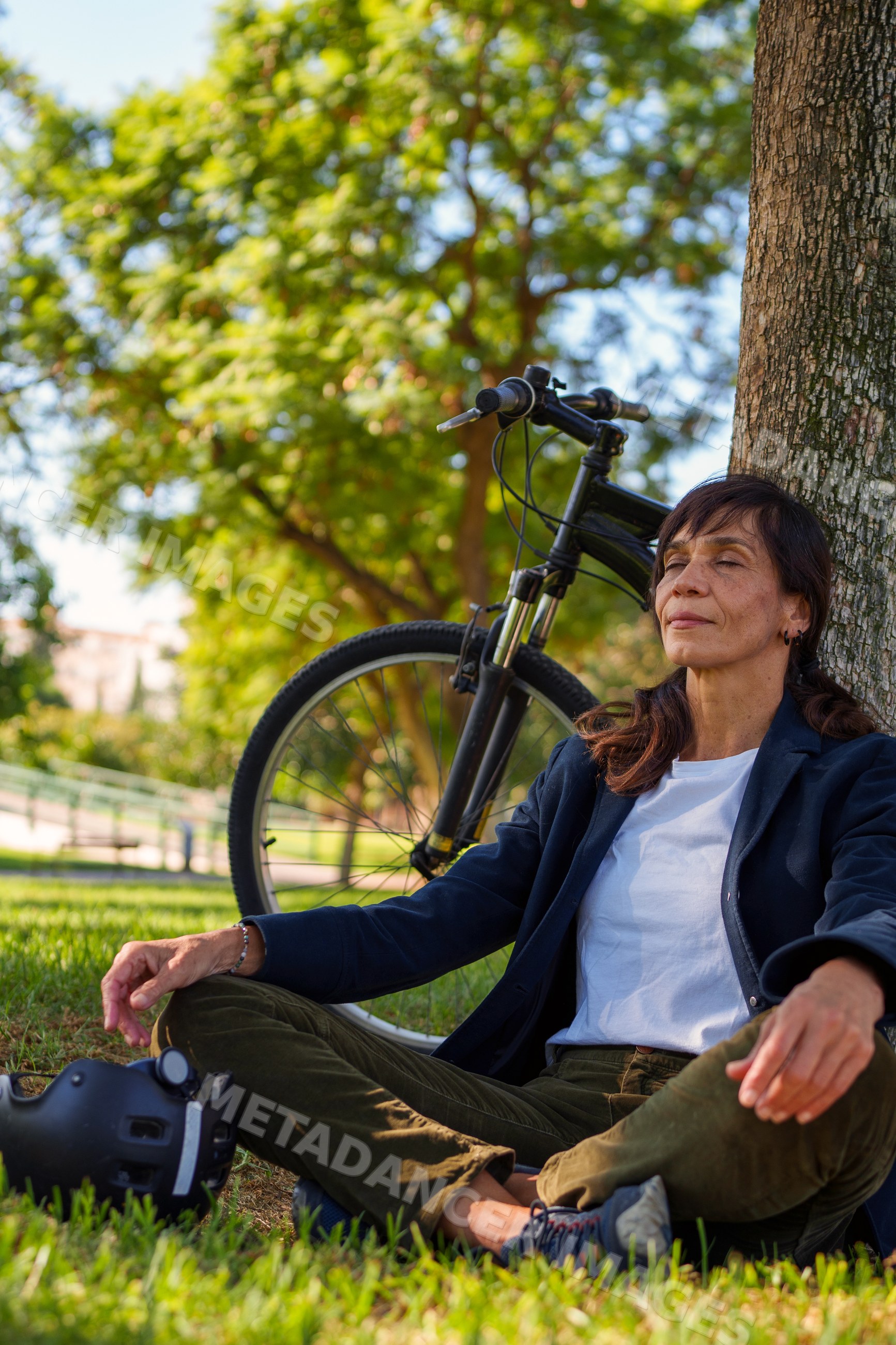 Hispanic woman resting against tree with bicycle in park in Málaga