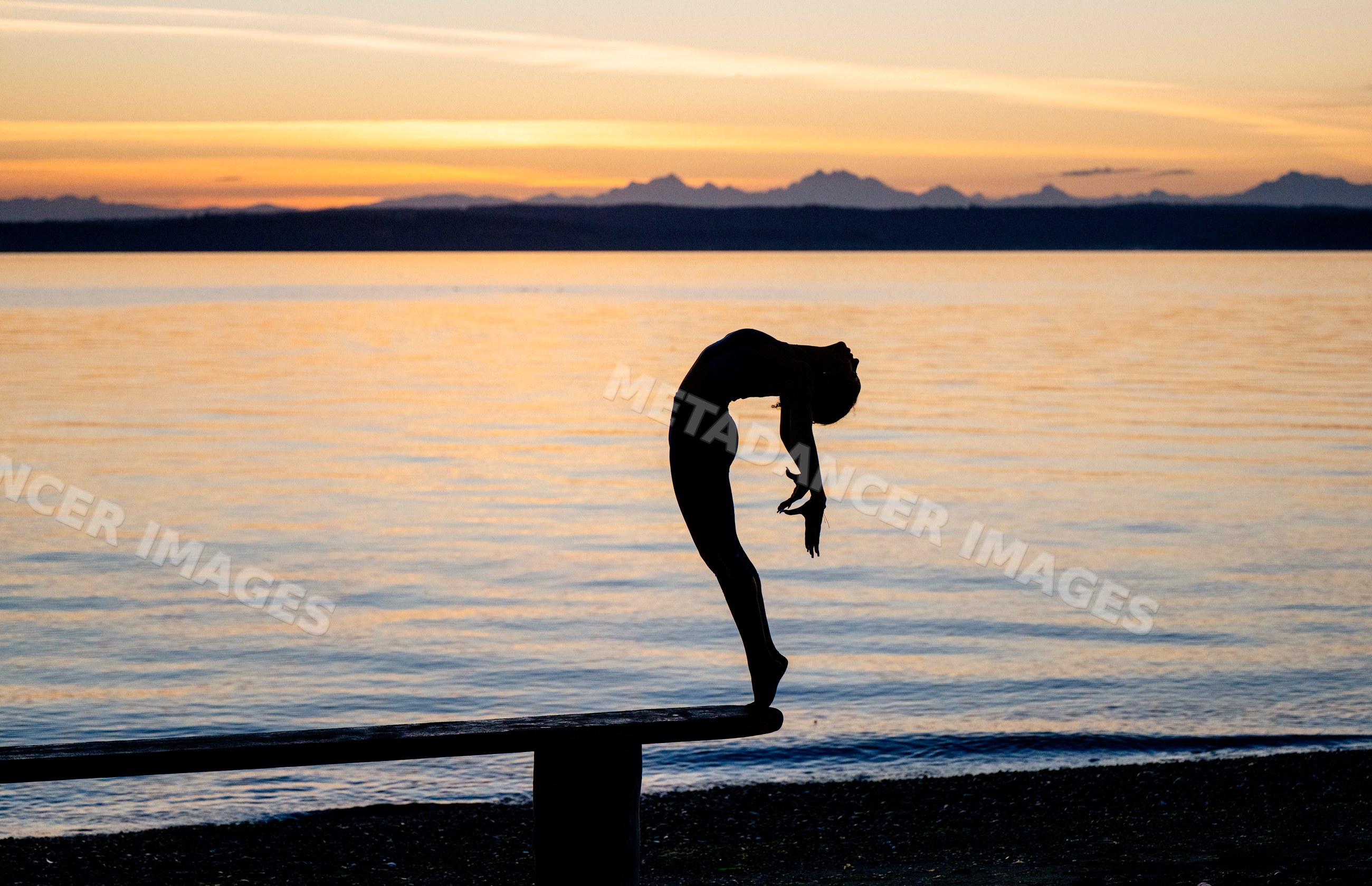 Hispanic woman performing backbend yoga pose on bench by water