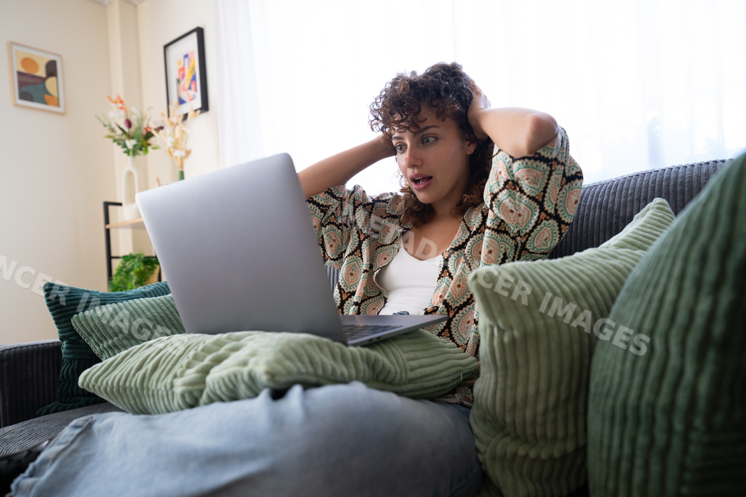 White woman using laptop on couch with surprised expression